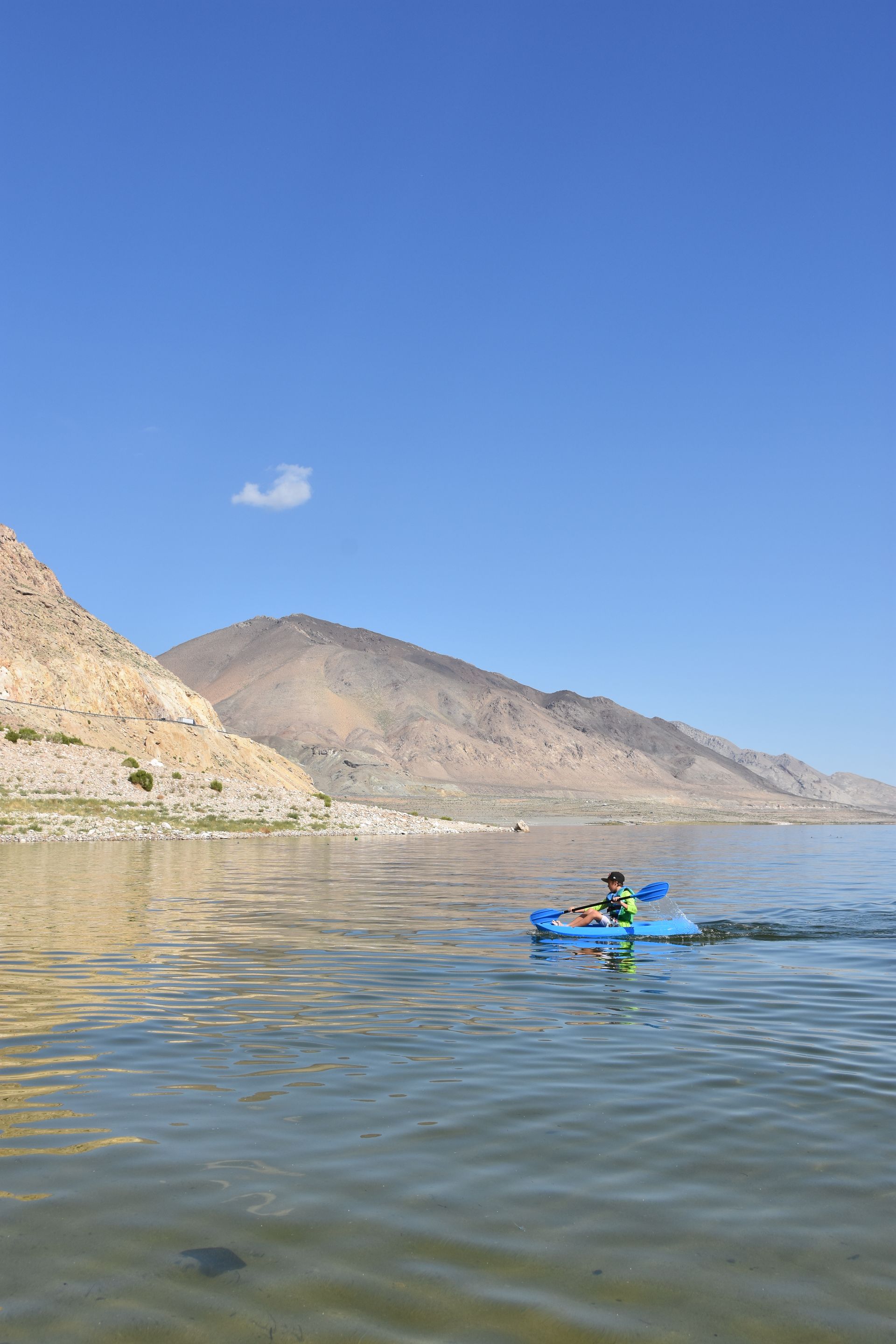 A person is riding a kayak on a lake with mountains in the background.