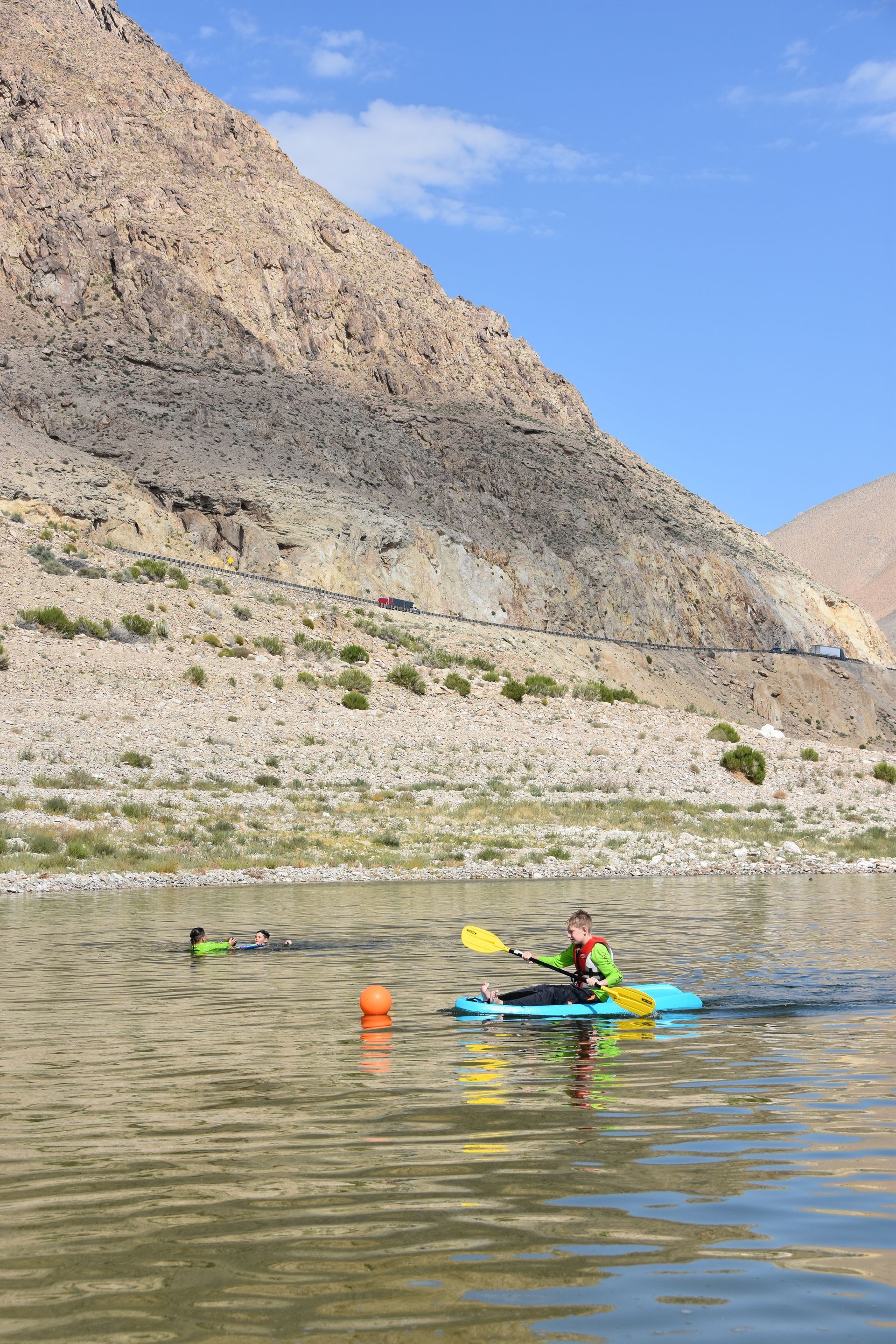 A man is paddling a kayak on a lake with mountains in the background.