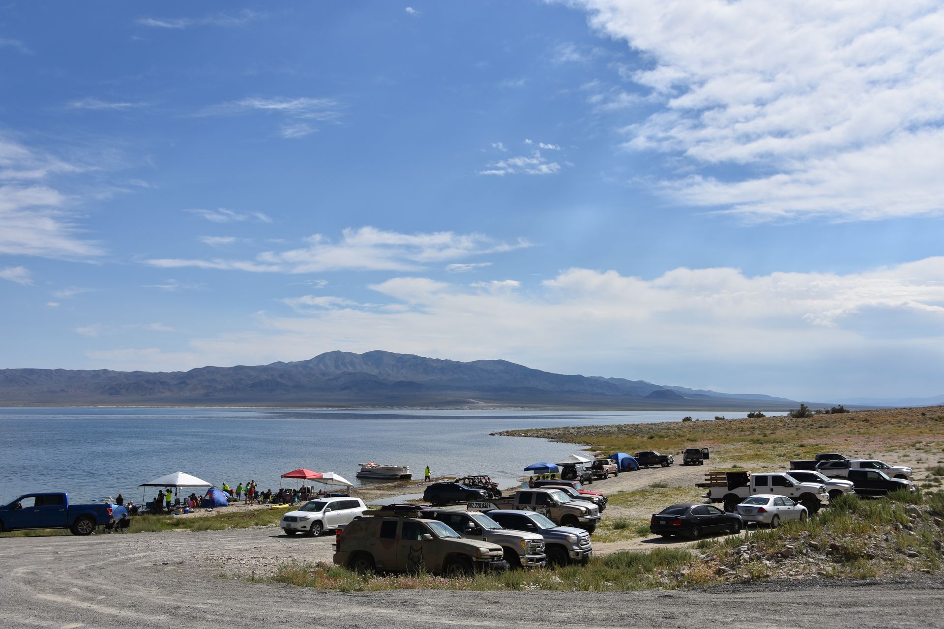 A lot of cars are parked on the shore of a lake.