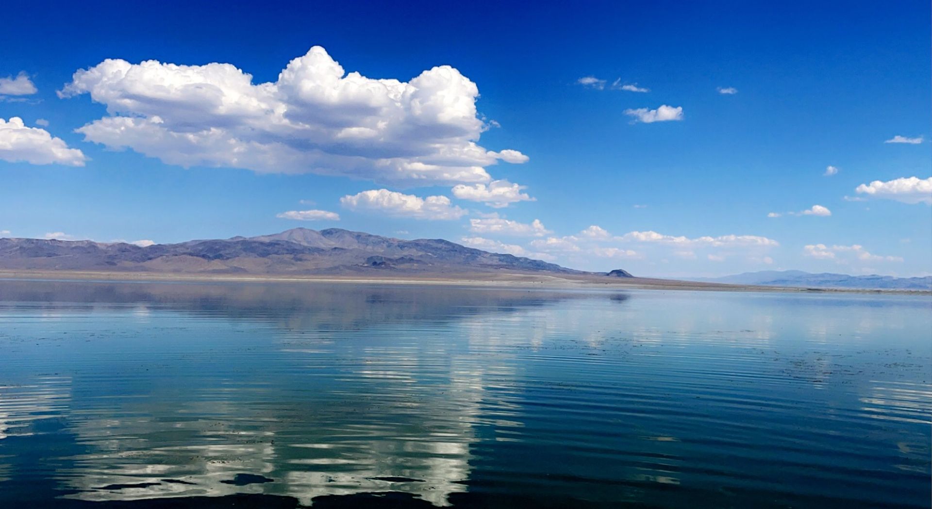 A lake with mountains in the background and clouds reflected in the water