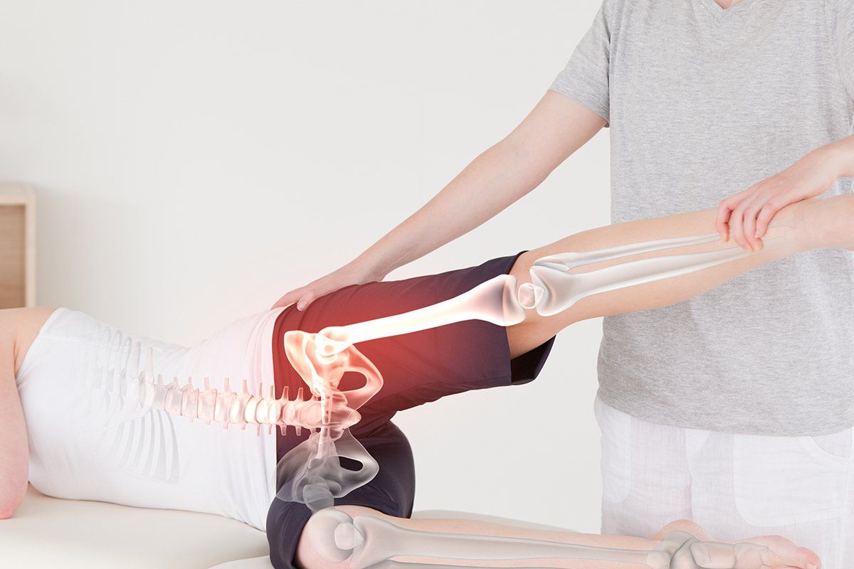 Therapist assesses patient's hip movement as they lay on the therapist's table.