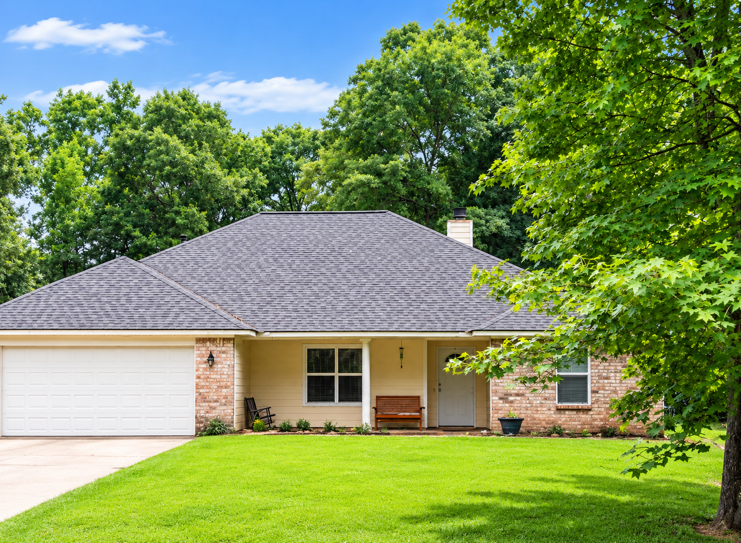 Single-story suburban house with white garage, gray roof, brick accents, and green lawn under a blue sky