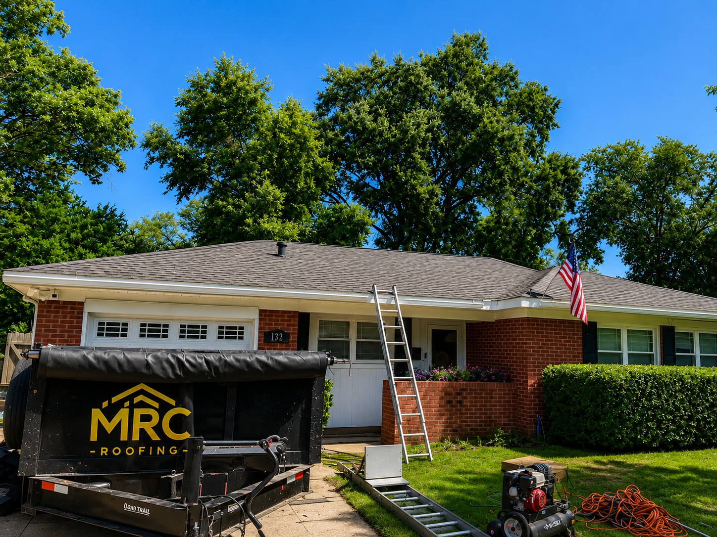 Single-story house with a black dump trailer in front and an American flag near the garage