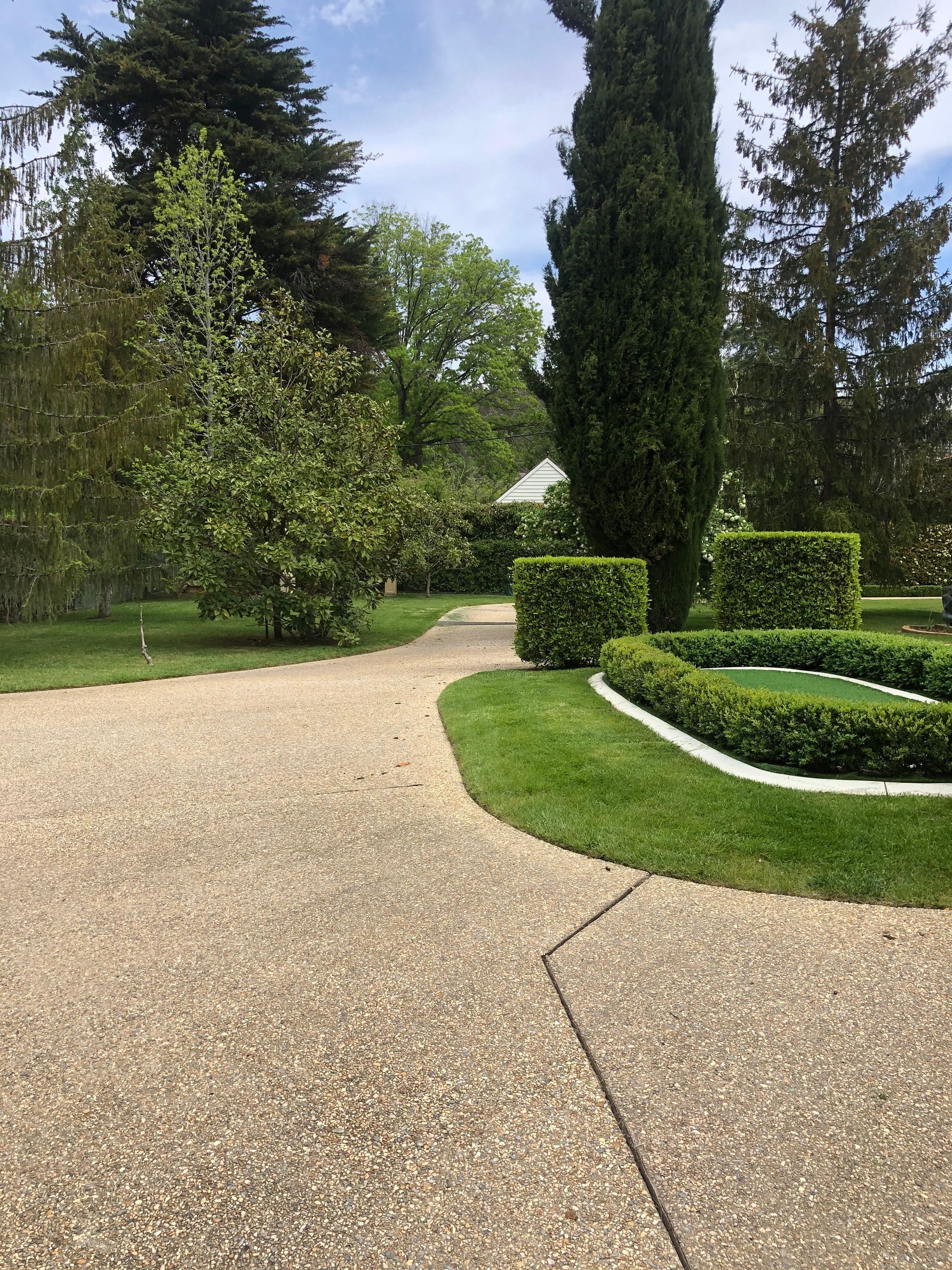 Curved gravel garden path beside trimmed hedges and tall trees under a cloudy sky