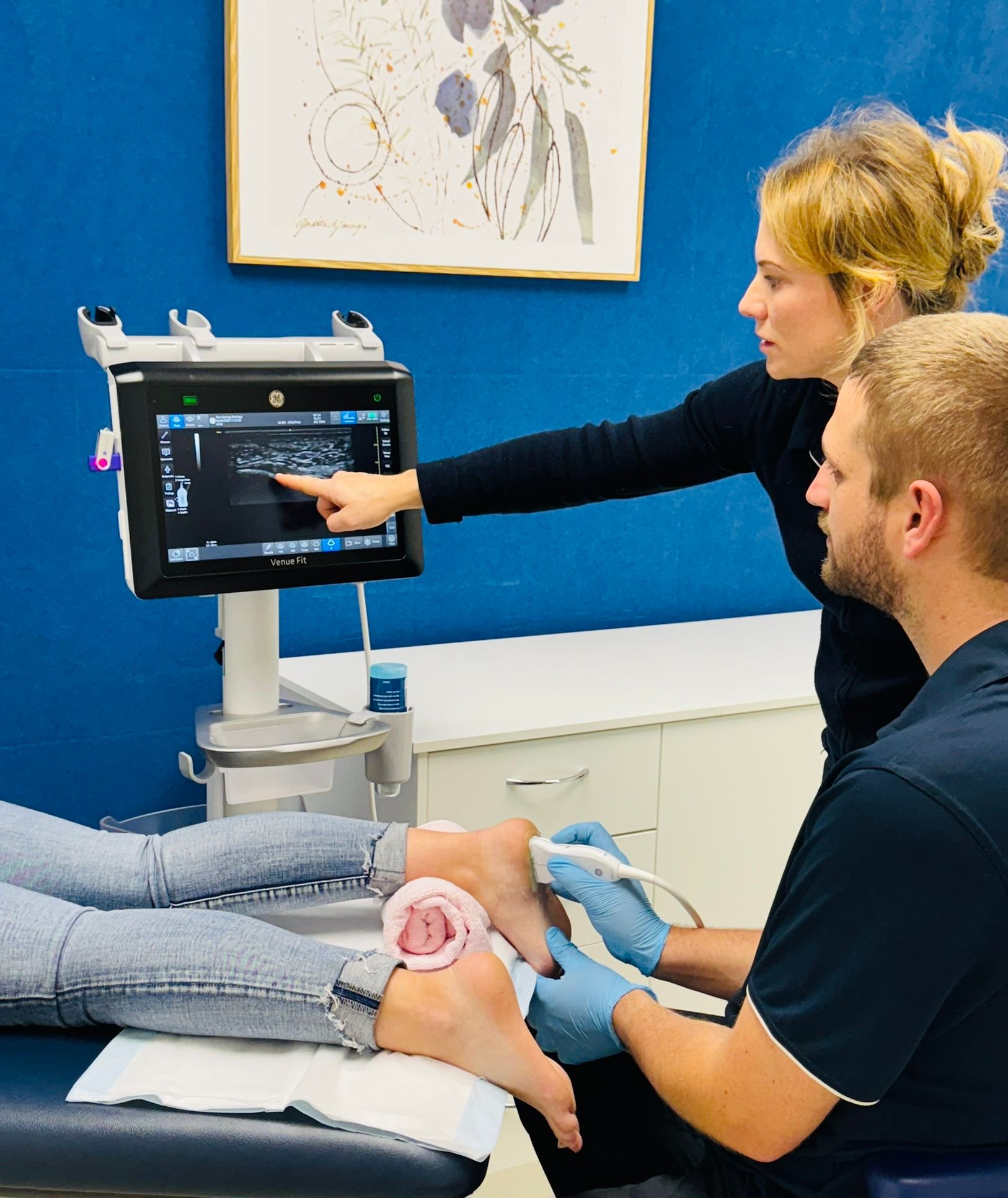 Two medical professionals perform a foot ultrasound, pointing at the screen. One patient's foot rests on a table in a medical setting. — Alice Springs Podiatry in Ciccone, NT