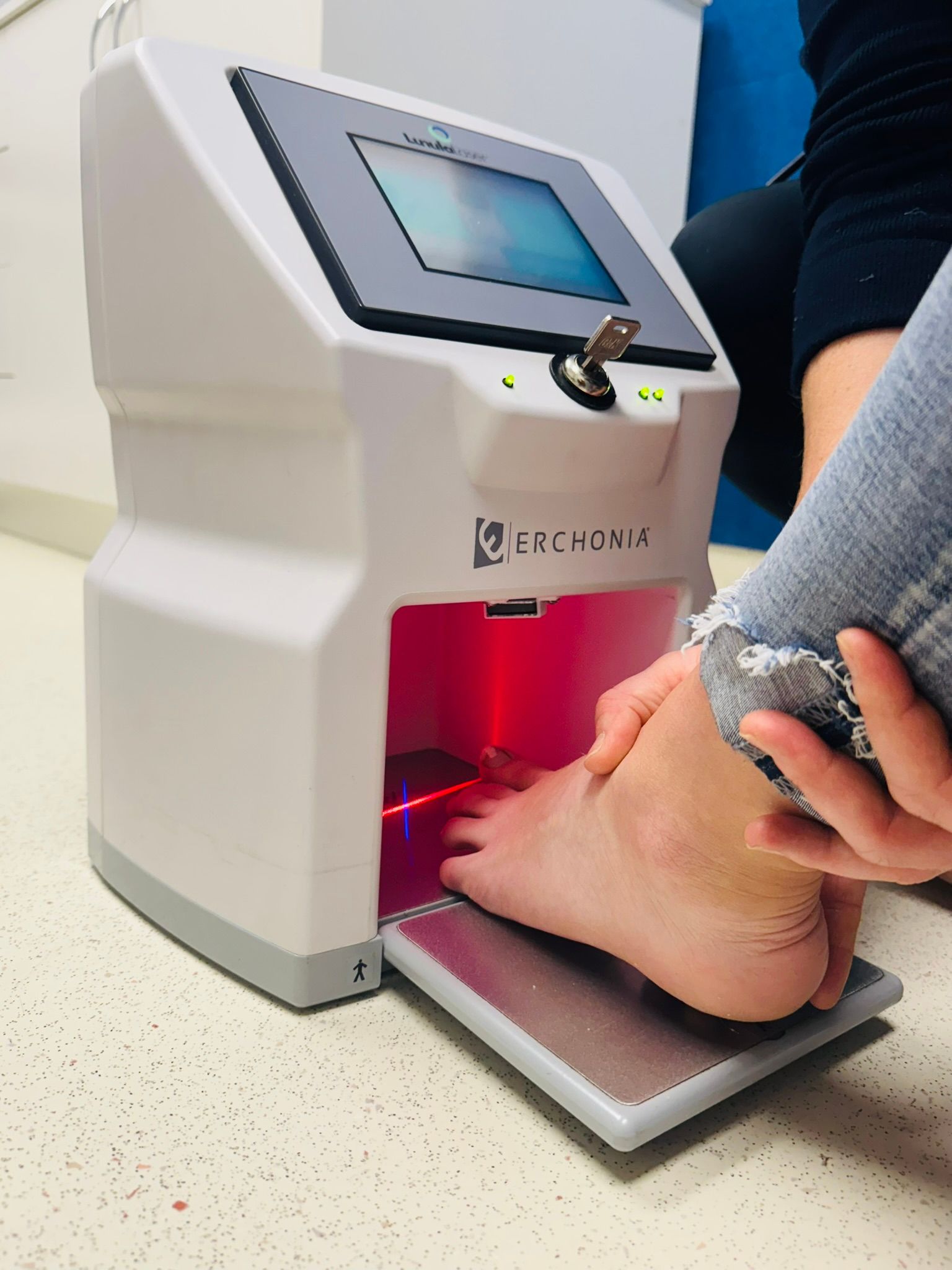 A person's foot being scanned by a white medical device with a red laser. The device has a screen and the person is seated. — Alice Springs Podiatry in Ciccone, NT