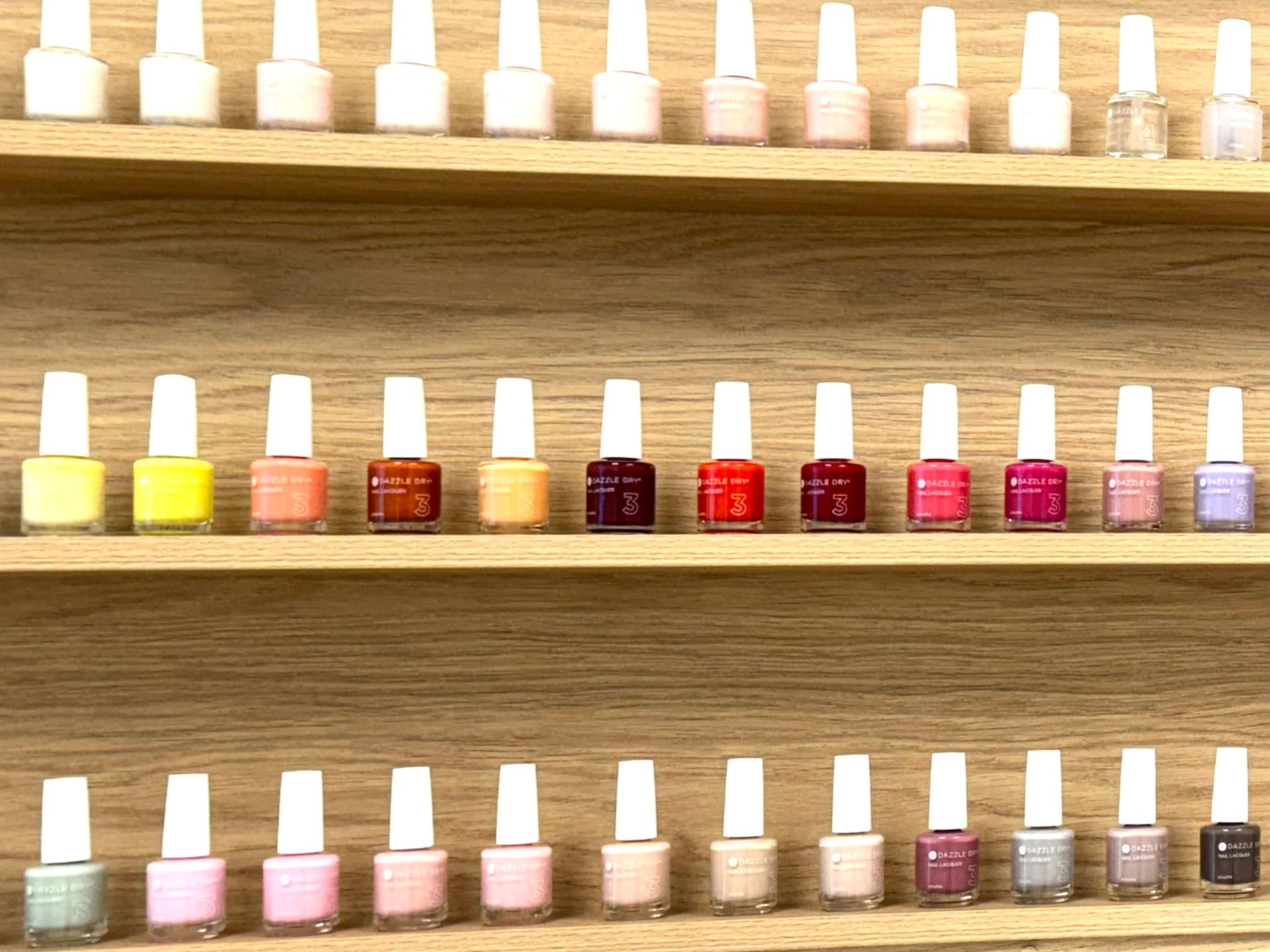 Nail polish bottles on wooden shelves, displaying a variety of colours like pinks, reds, and neutrals. — Alice Springs Podiatry in Ciccone, NT