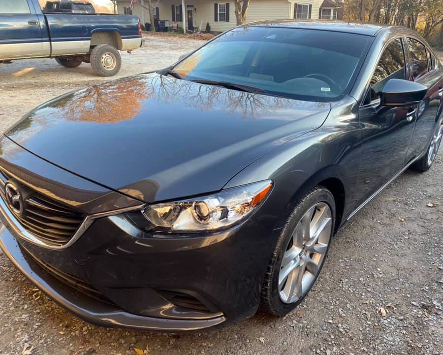 a black mazda 6 is parked in a gravel lot next to a truck .