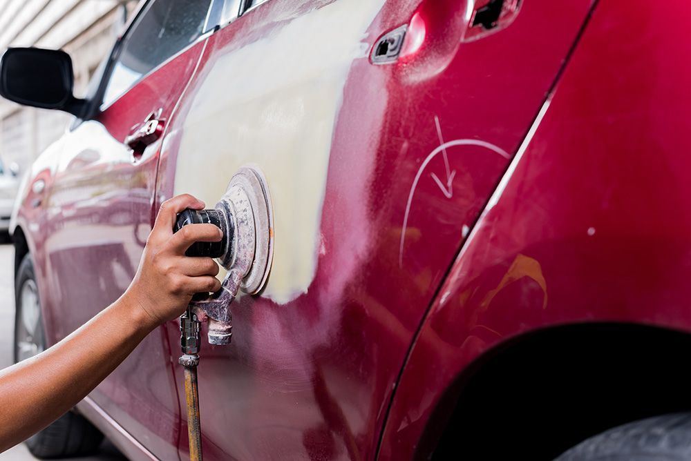 a person is sanding a red car with a sander .