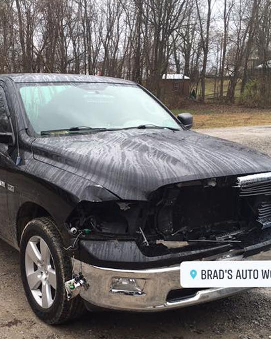 a black ram truck with a damaged hood is parked in a parking lot .