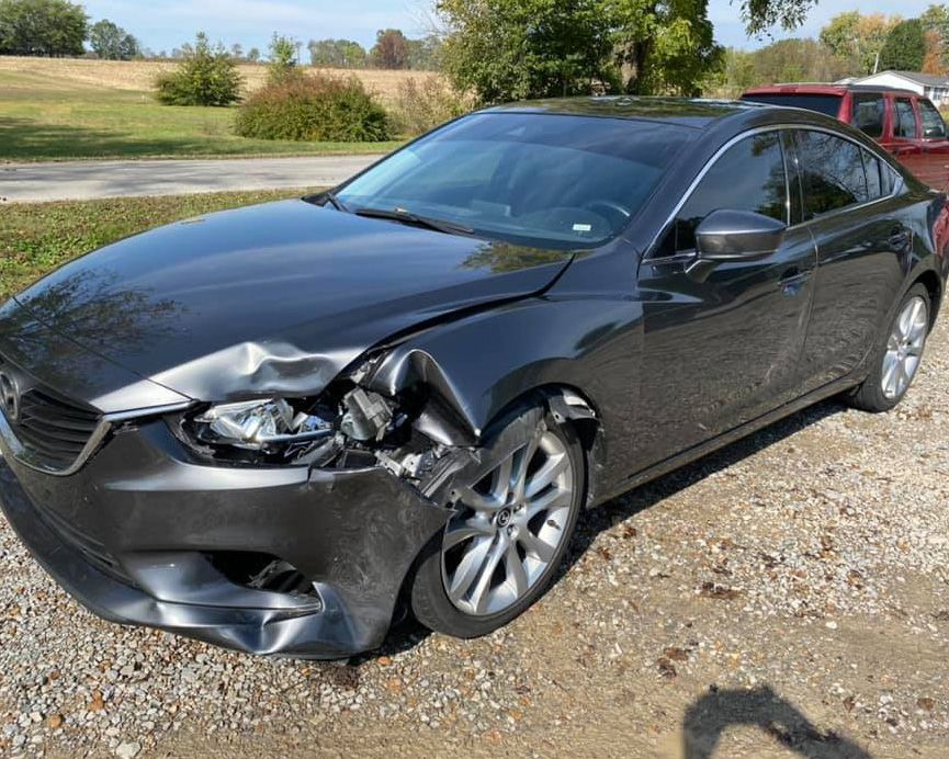 a black car with a damaged front end is parked in a gravel lot .