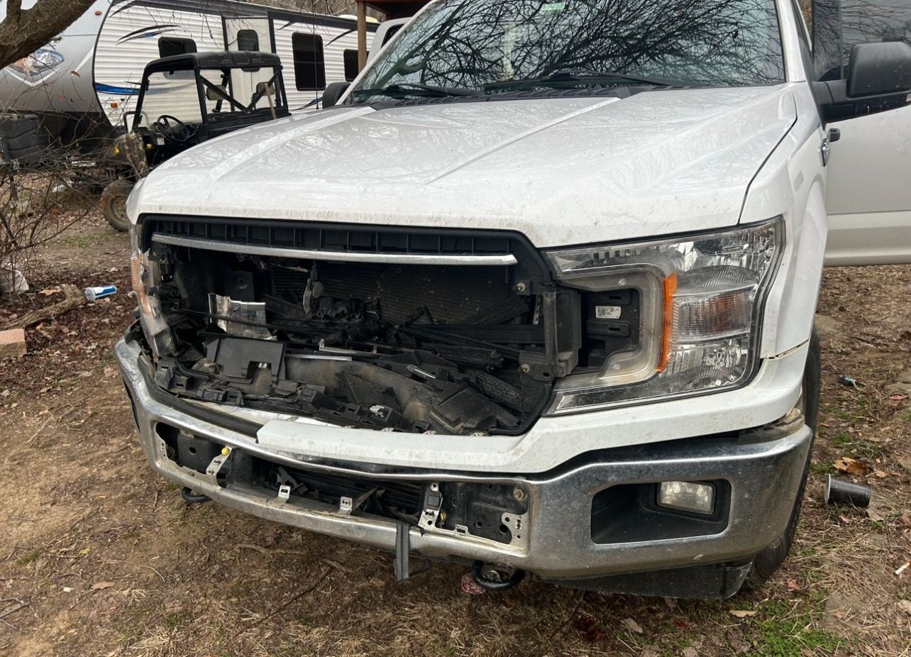 a black car with a damaged front end is parked in a gravel lot .