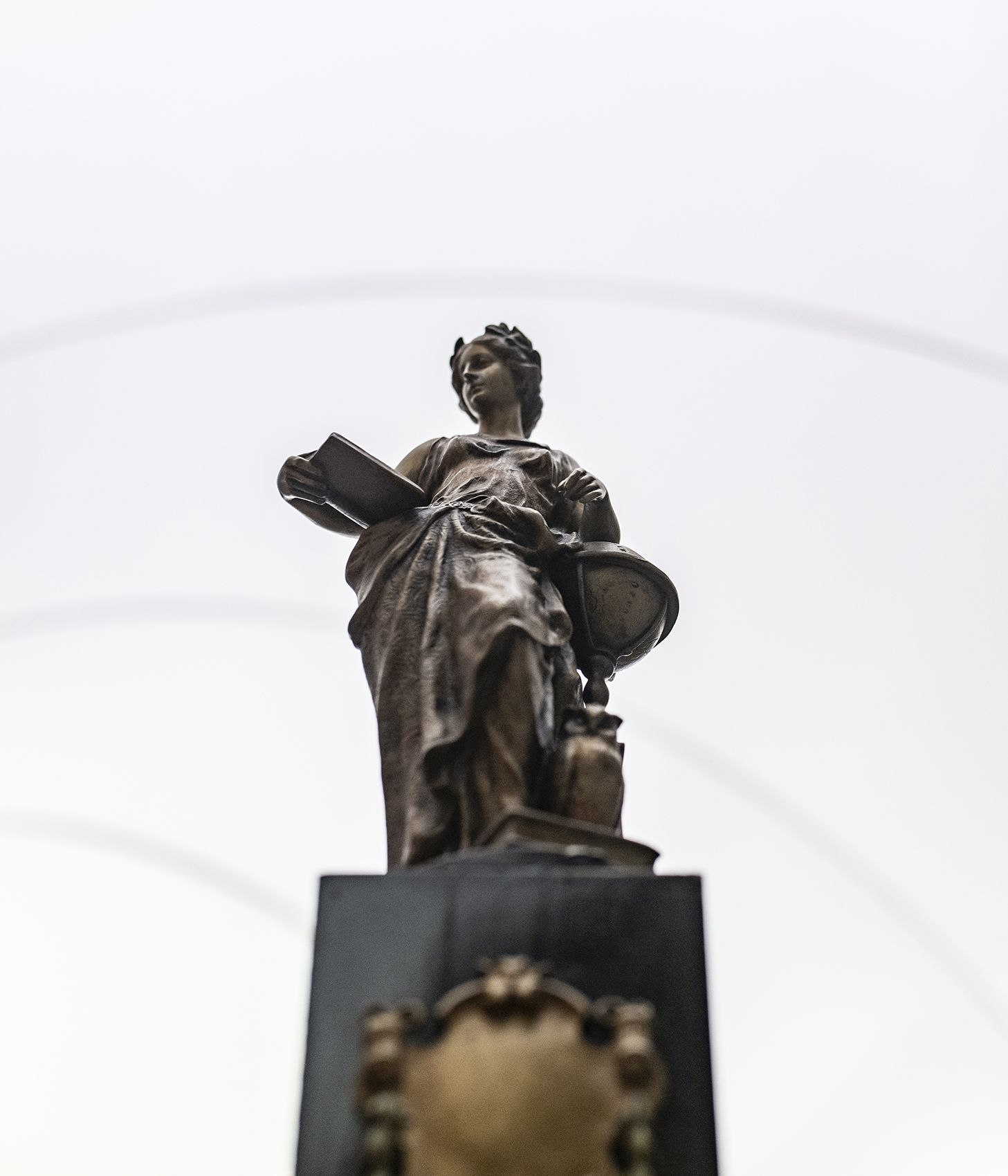 Bronzestatue auf einem Sockel, von unten vor einem hellen Himmel betrachtet.