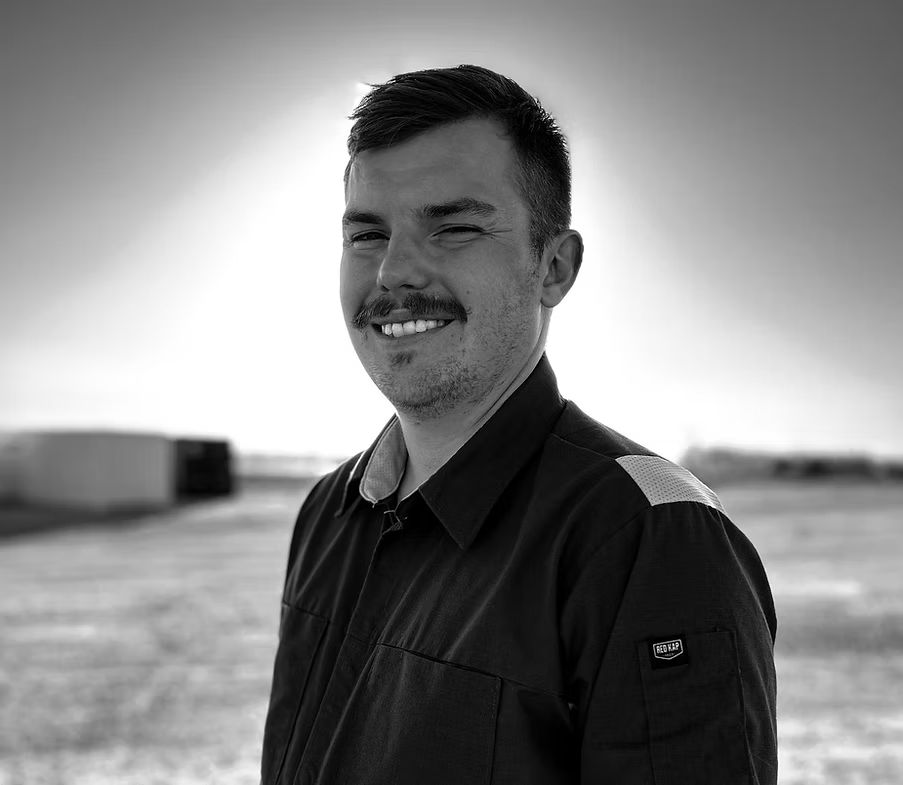 Smiling man in a dark jacket standing outdoors in a black-and-white portrait