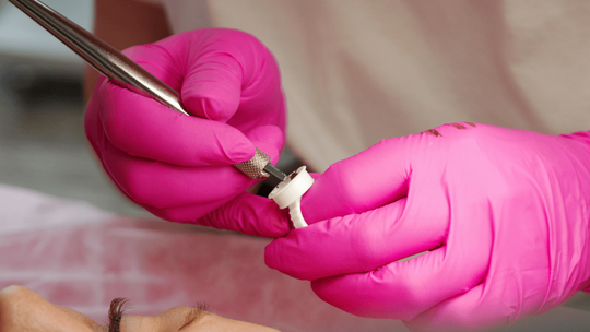 Technician wearing bright pink gloves carefully performing detailed eyebrow microblading with a precision tool during a microblading service in Spanish Fork, UT