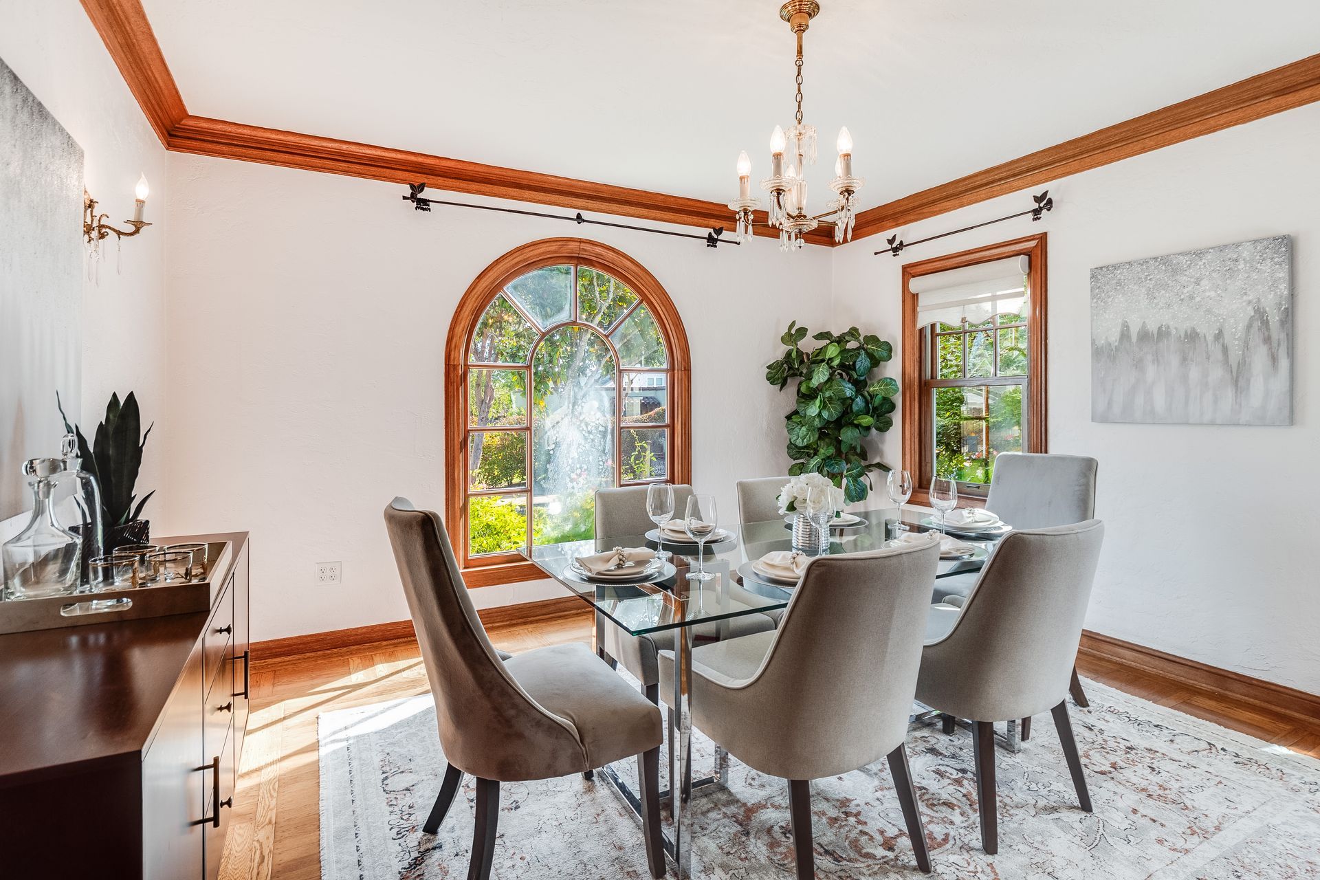 Bright dining room with a large table, upholstered chairs, arched window, and chandelier on a rug