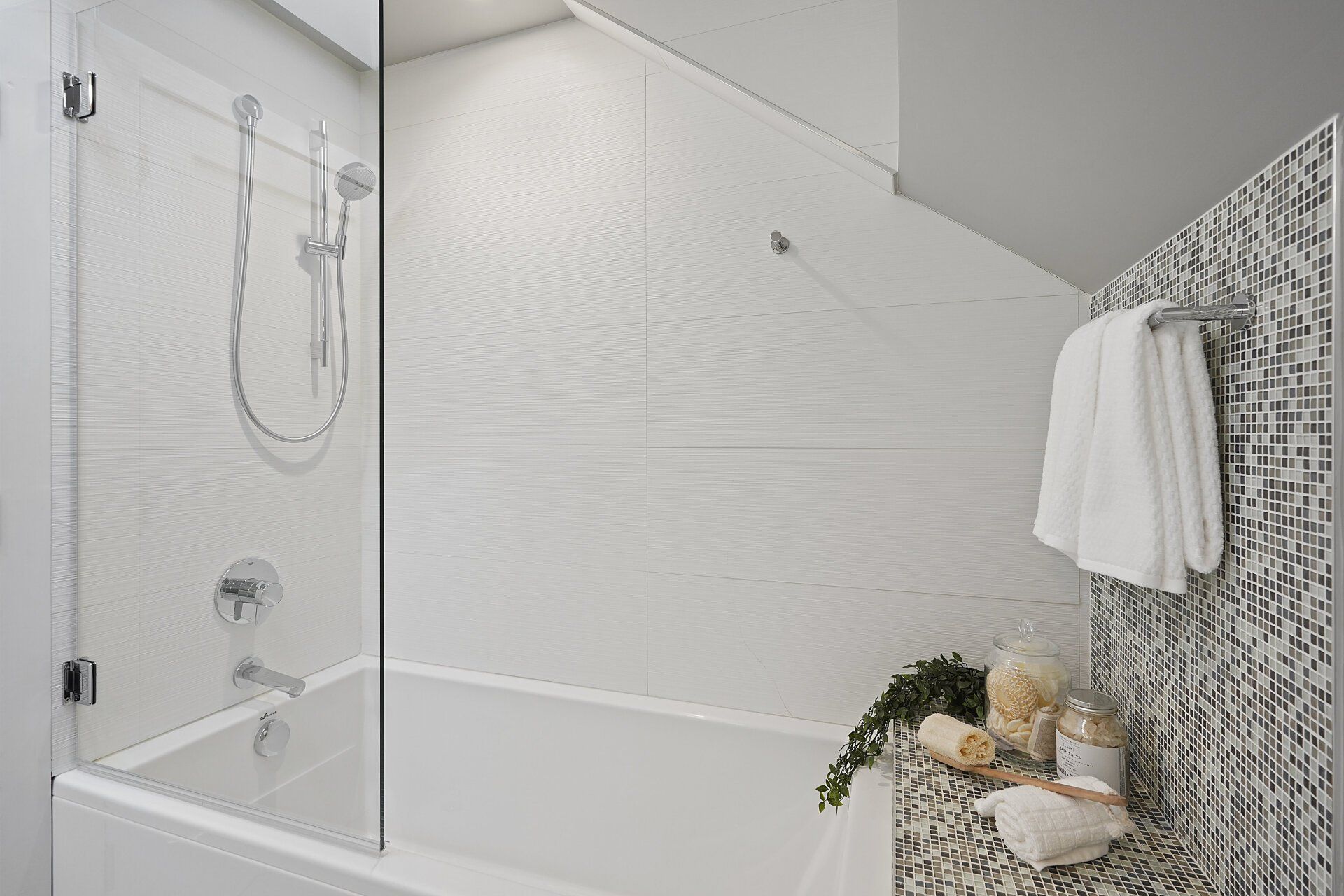 Bright bathroom with glass shower door, tub, and patterned accent wall. Towels hang from a silver bar.