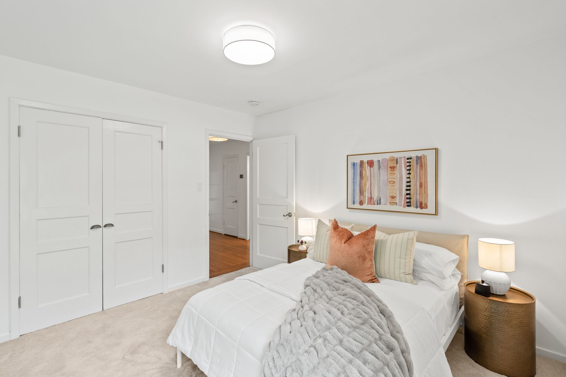 A bedroom with a bed , nightstands , lamps and a picture on the wall.