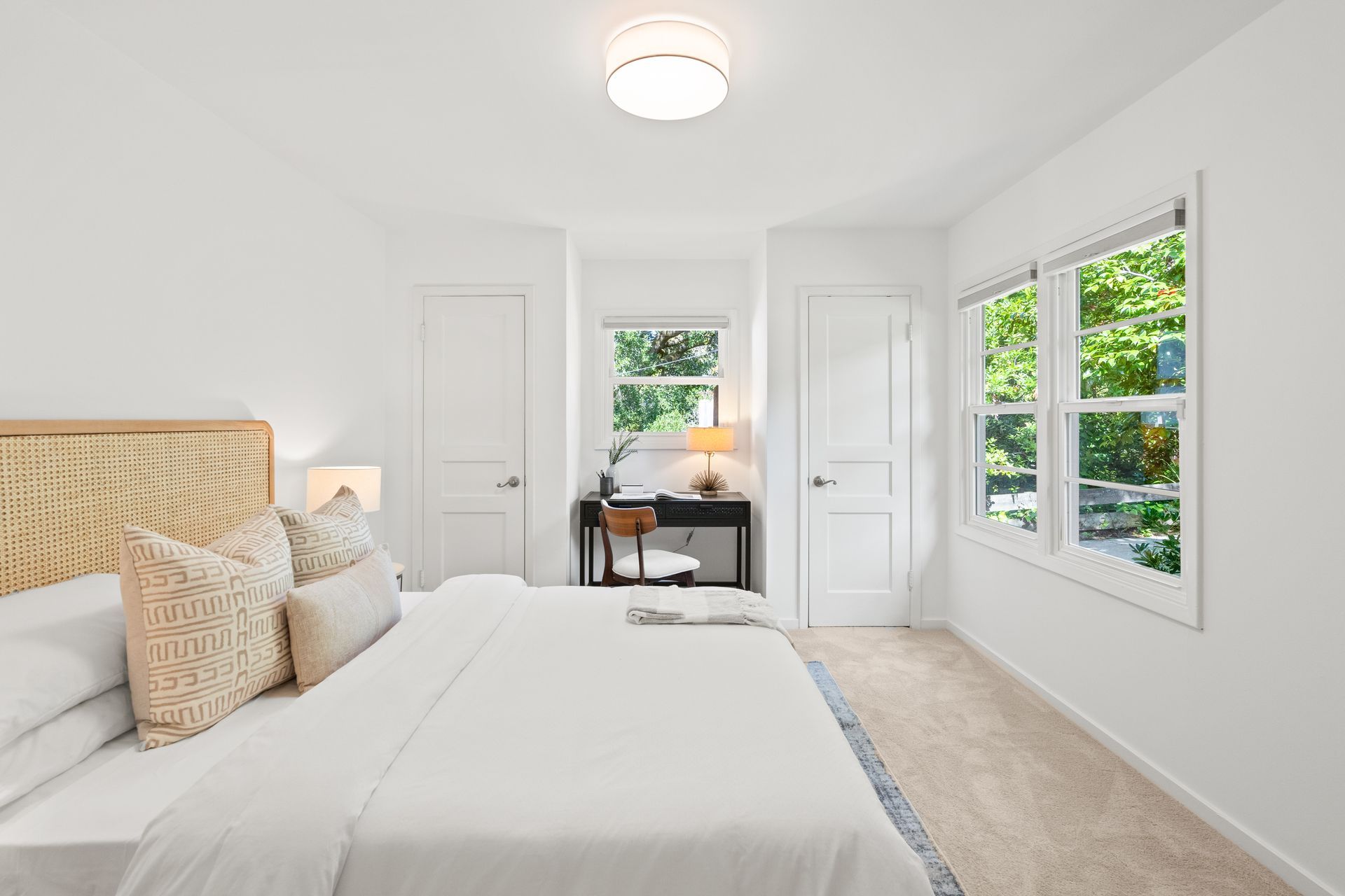 A bedroom with a bed , desk , and two windows.