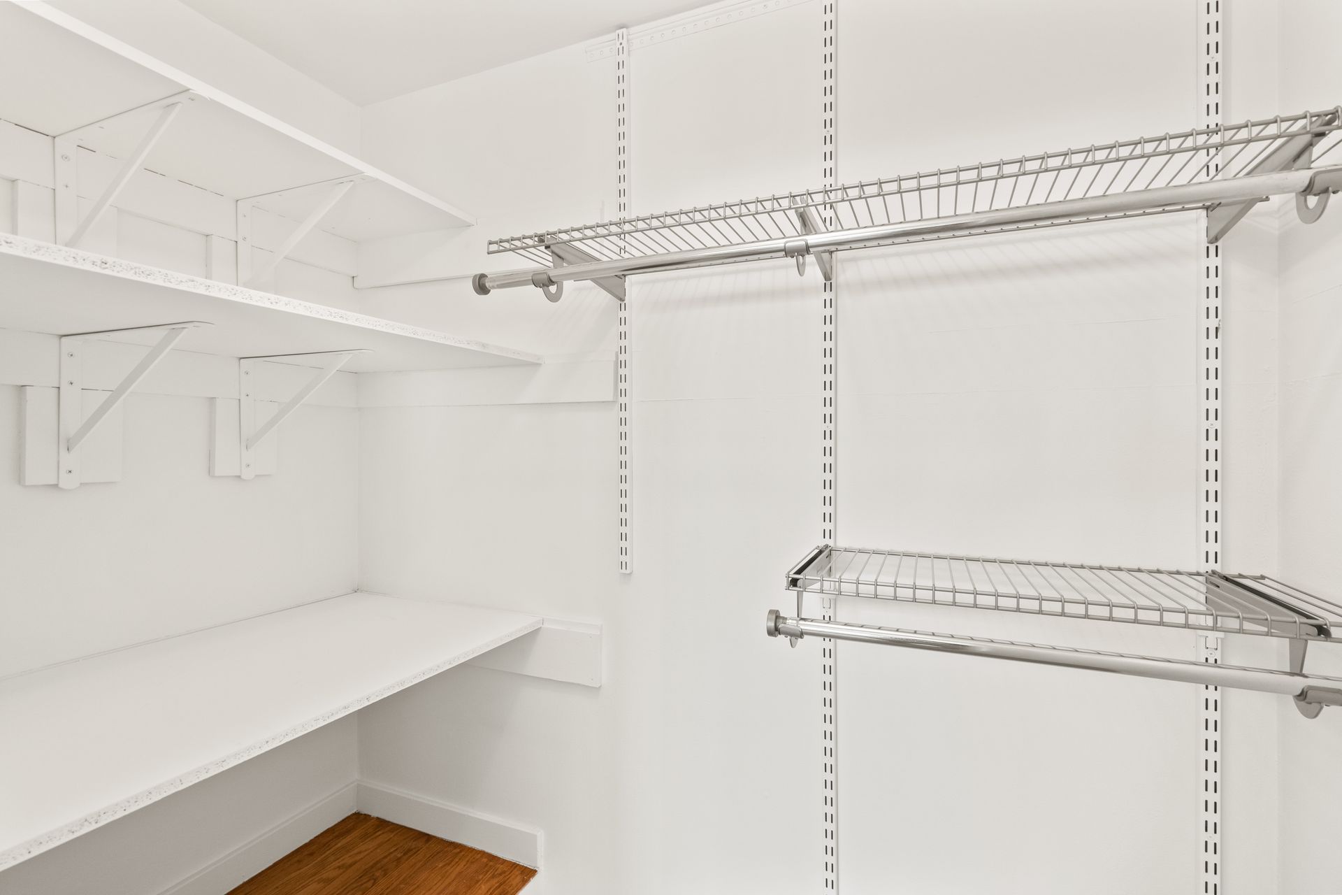 An empty walk in closet with white shelves and a wooden floor.