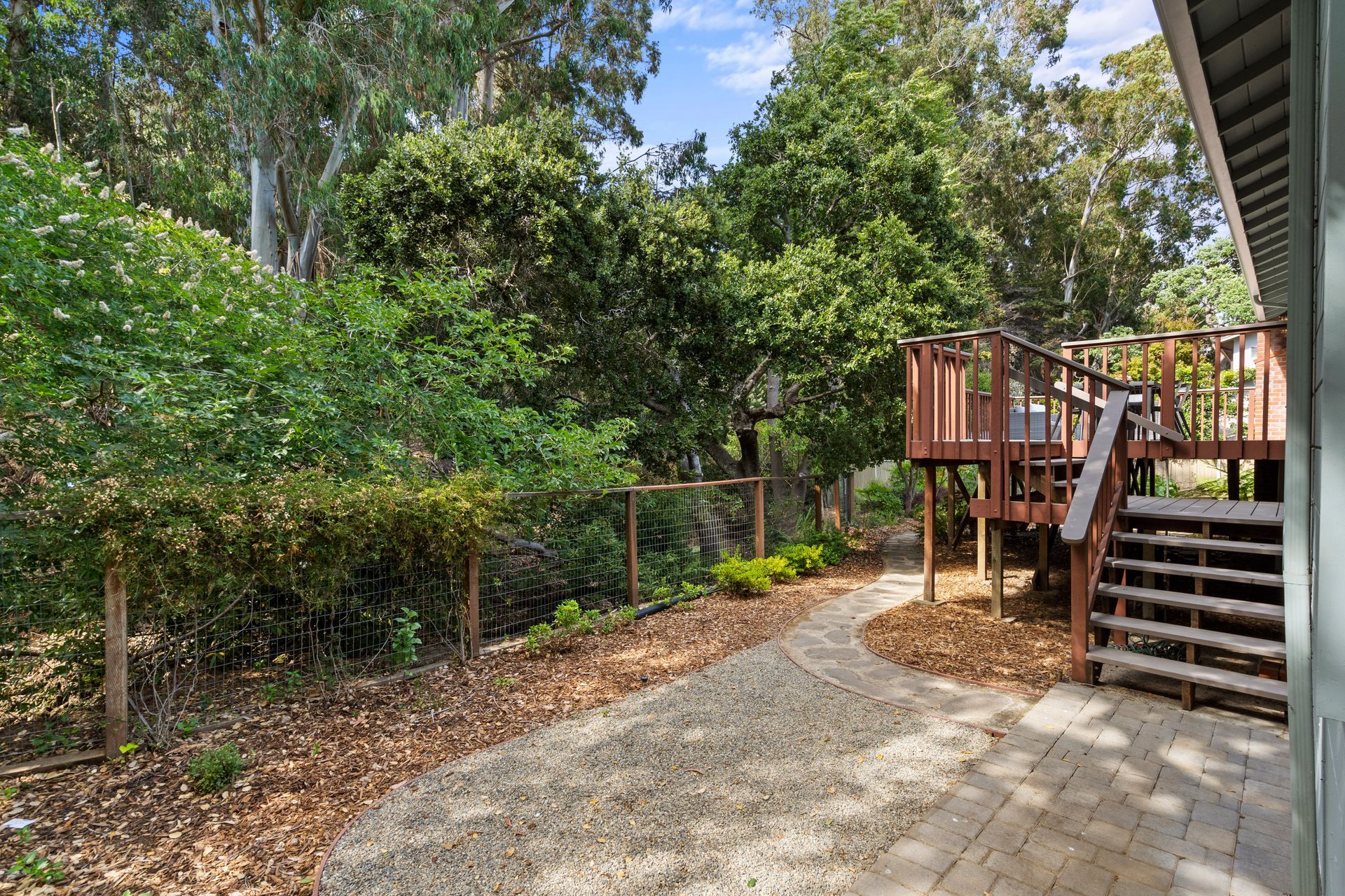 A house with a deck and stairs in the backyard surrounded by trees.