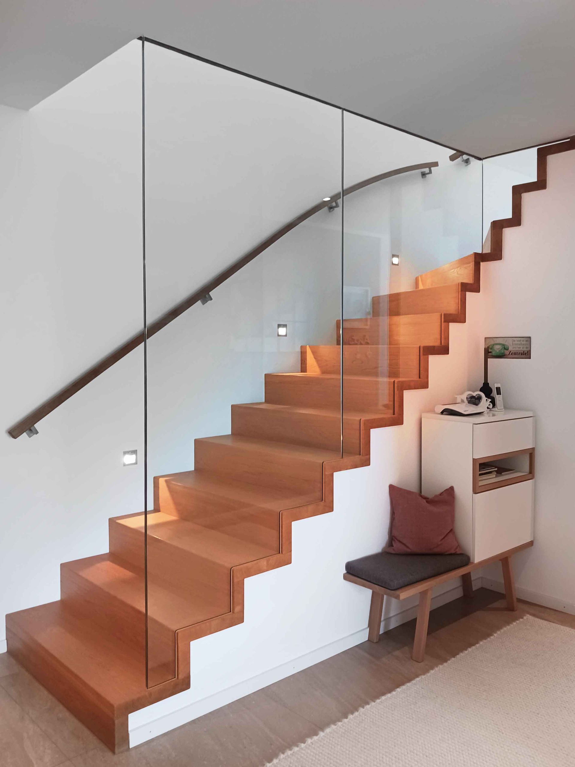 Moderne Holztreppe mit Glasgeländer in einer hellen Innenecke