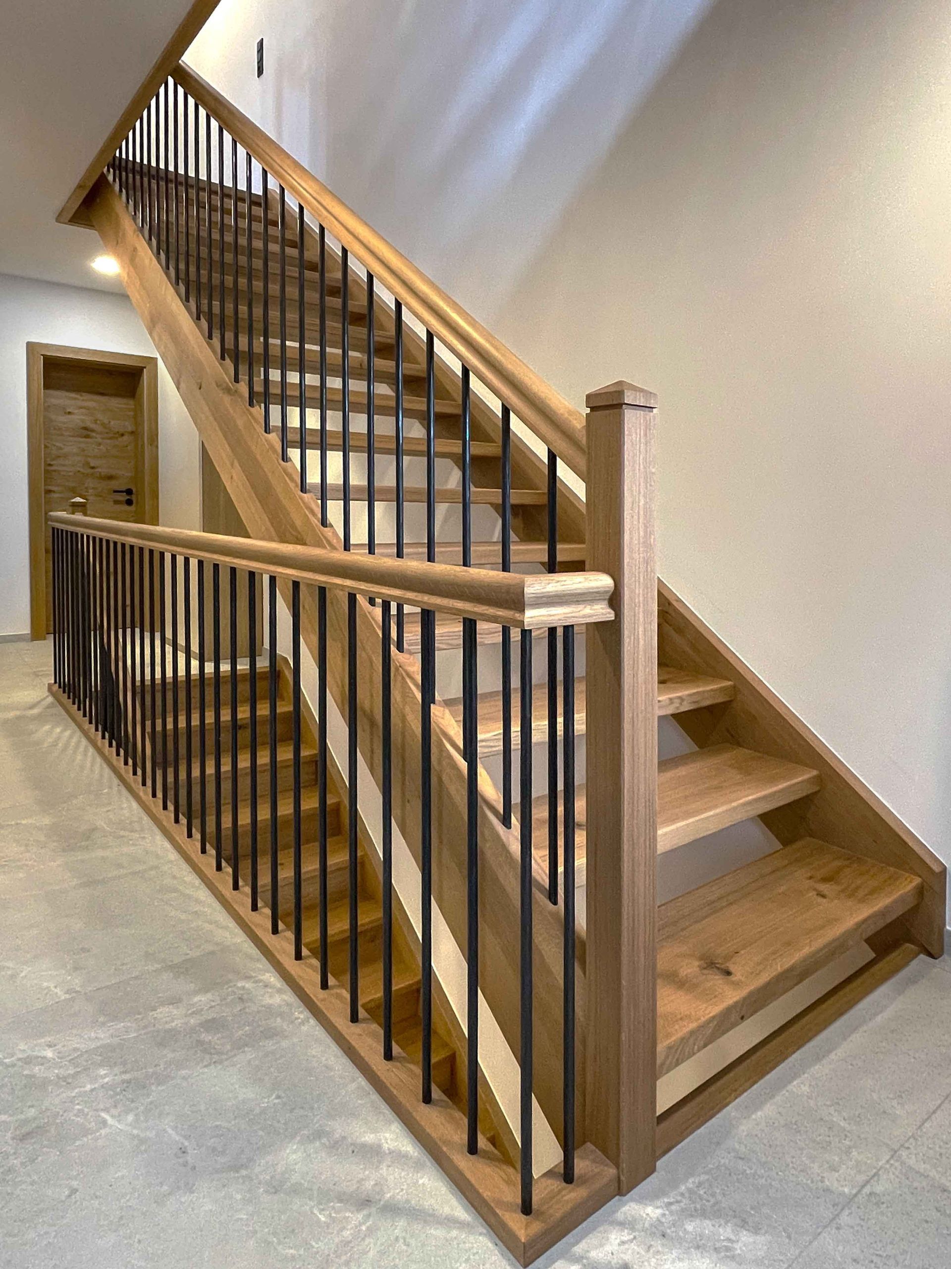 Holztreppe mit schwarzen Metallbalustern und Handläufen in einem Treppenhaus