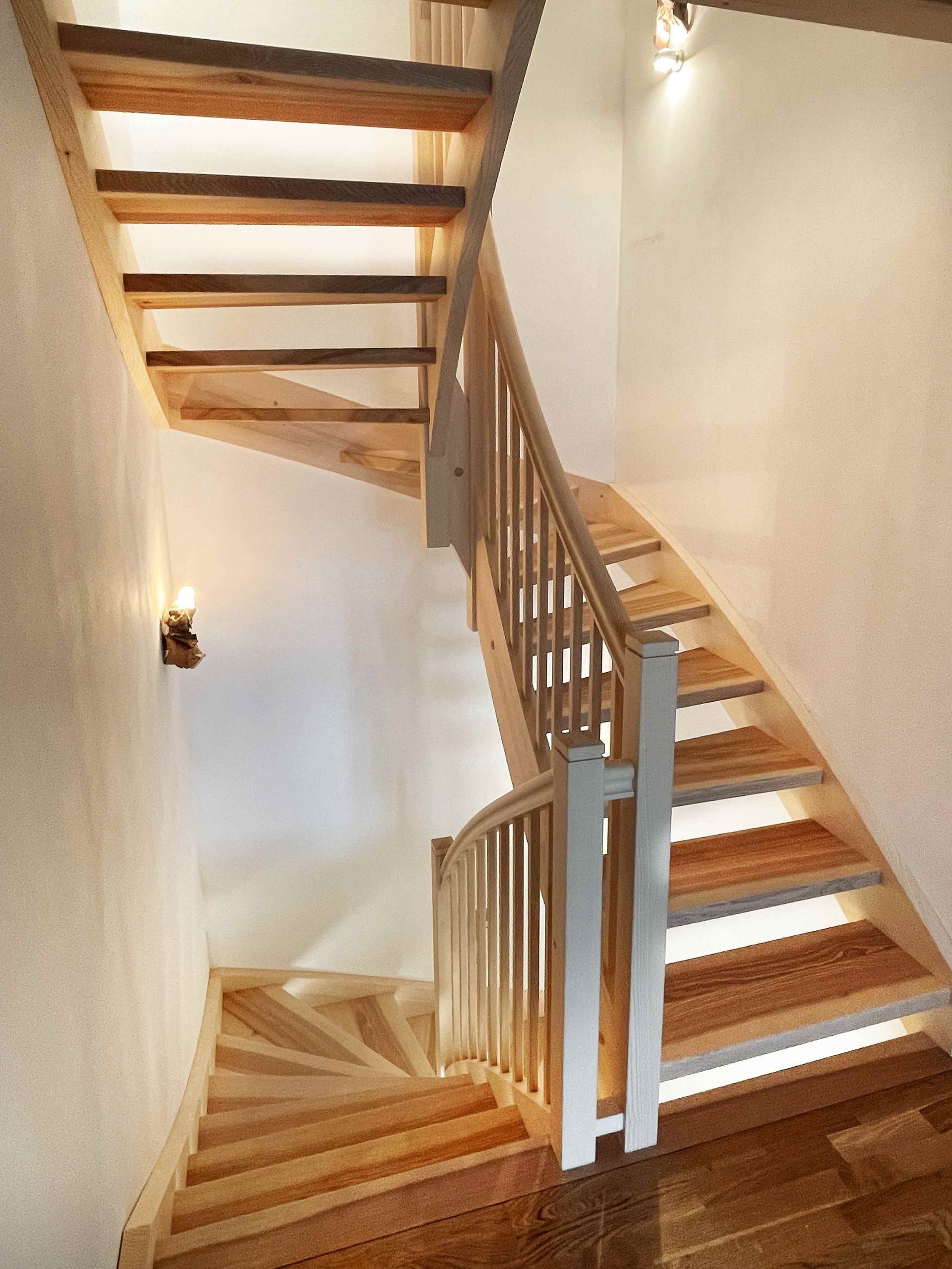 Holztreppe mit offenen Stufen und weißen Wänden in einem schmalen Flur