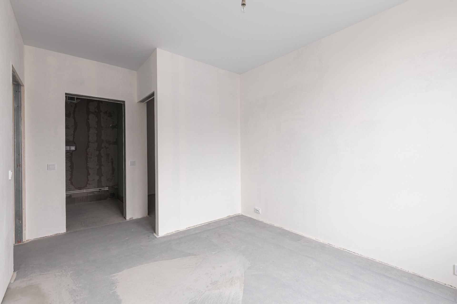 Empty white room with open doorway, unfinished gray floor, and minimal lighting
