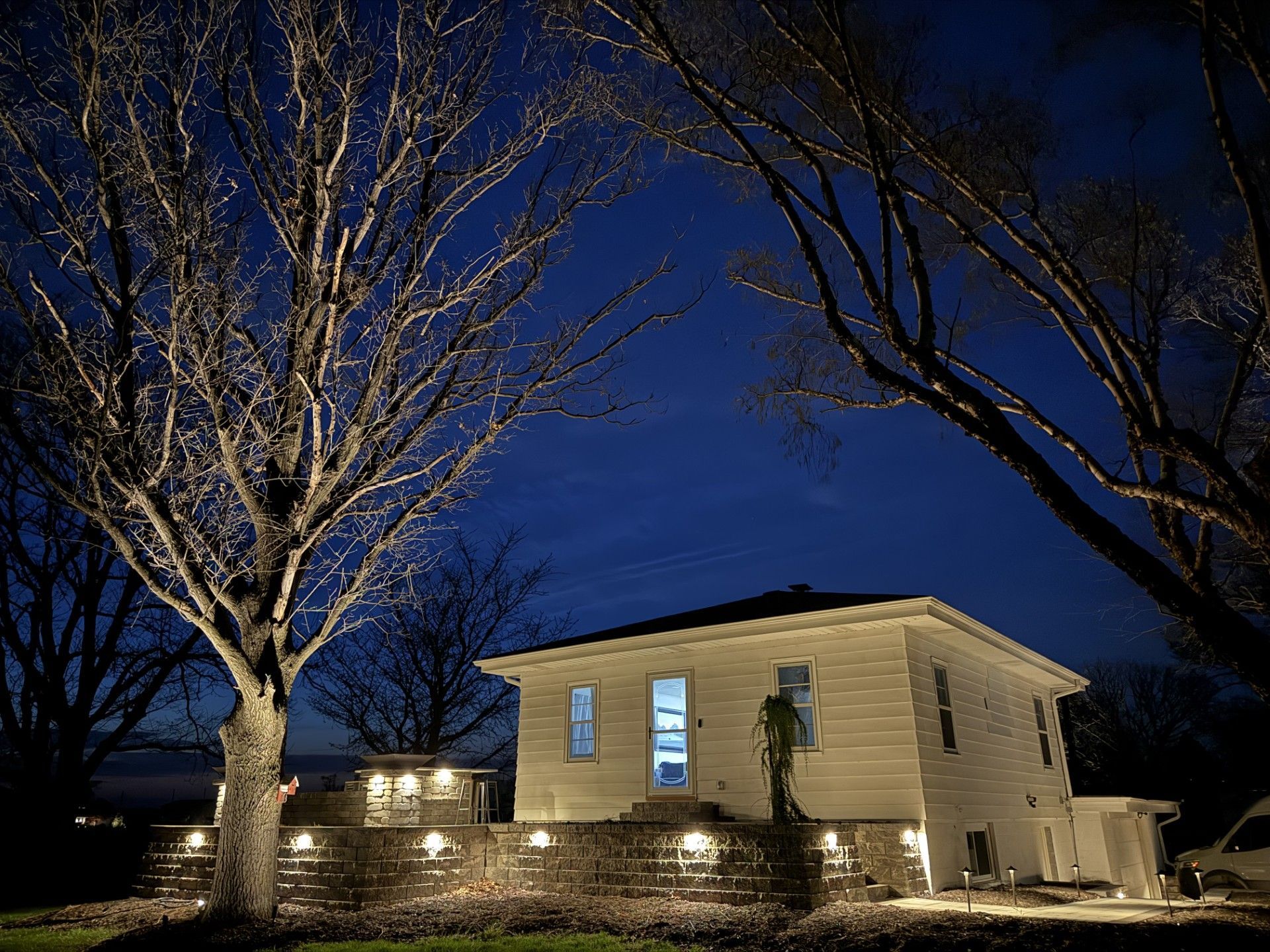 Nighttime view of a lit house with leafless trees under a deep blue sky