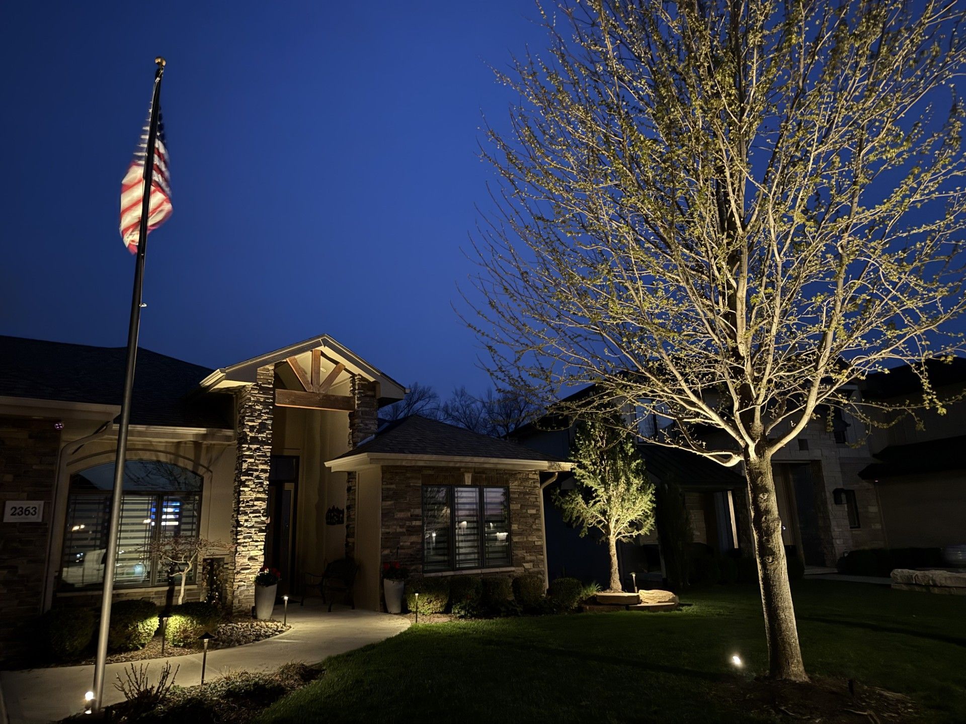 Lit-up brick building at dusk with an American flag and illuminated trees in front
