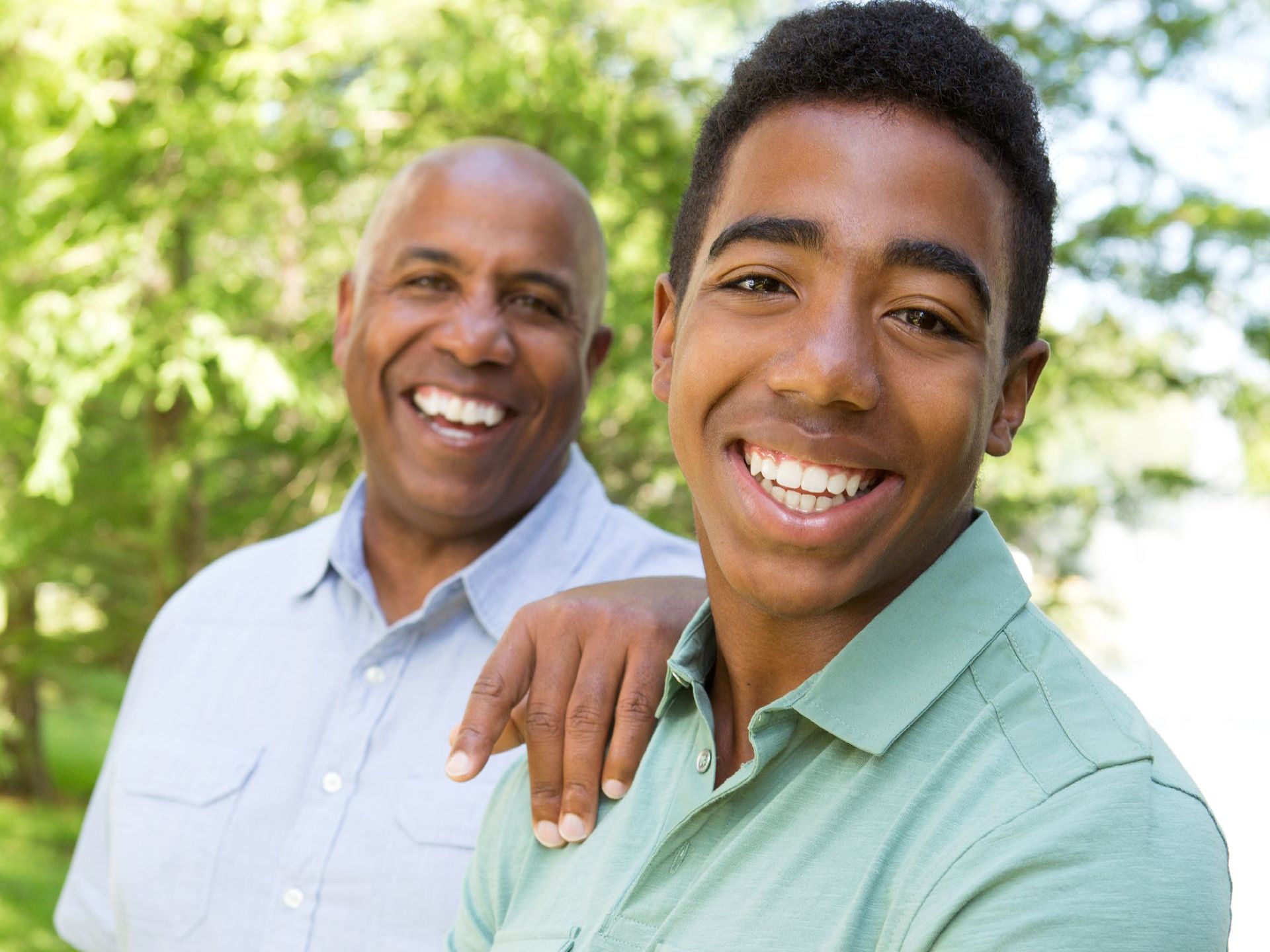 A man and a young man are posing for a picture in a park.