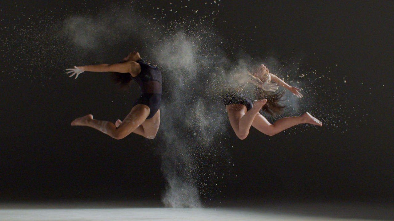 Two dancers are jumping in the air with powder coming out of them.