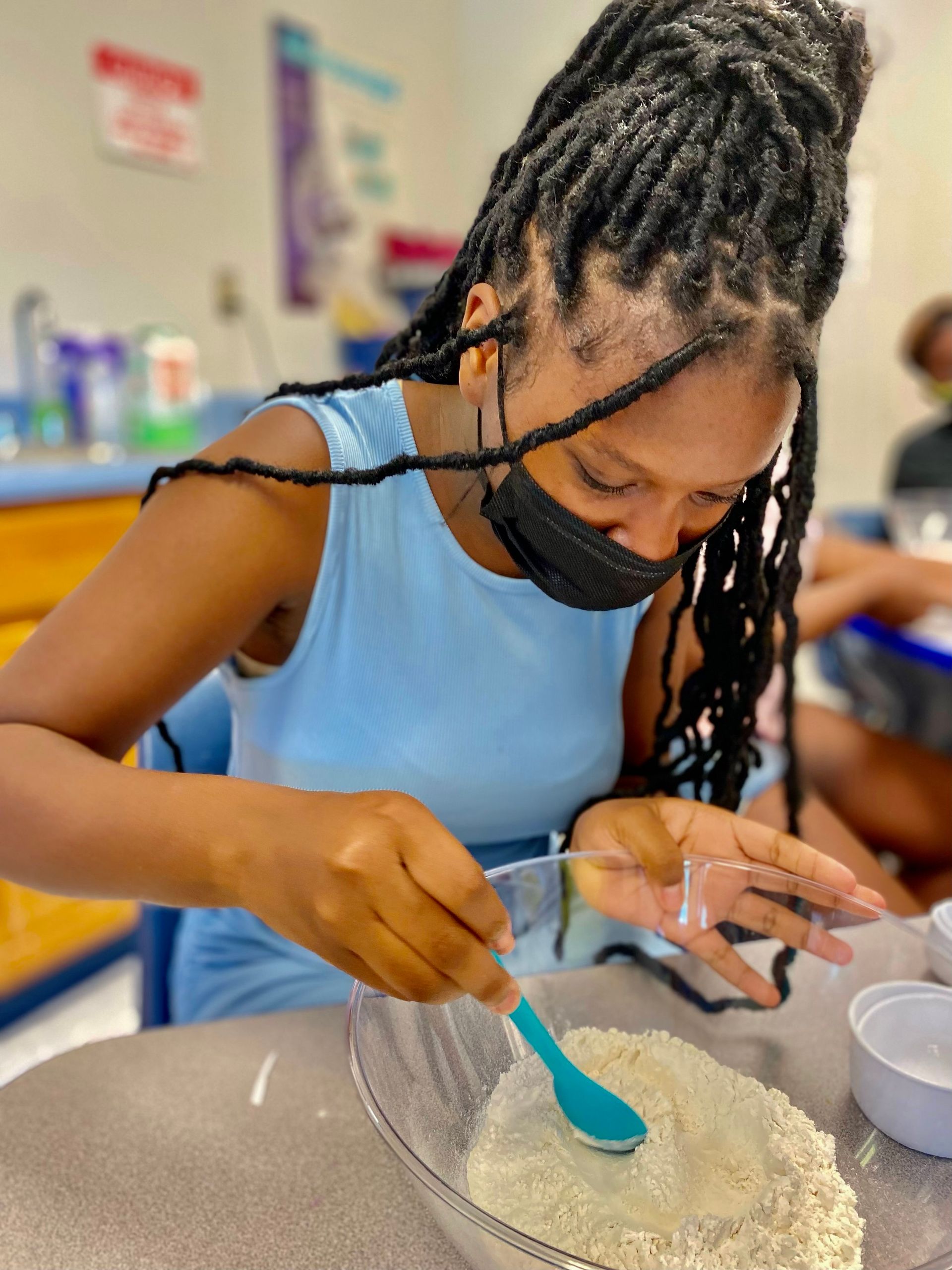 A girl wearing a mask is mixing something in a bowl