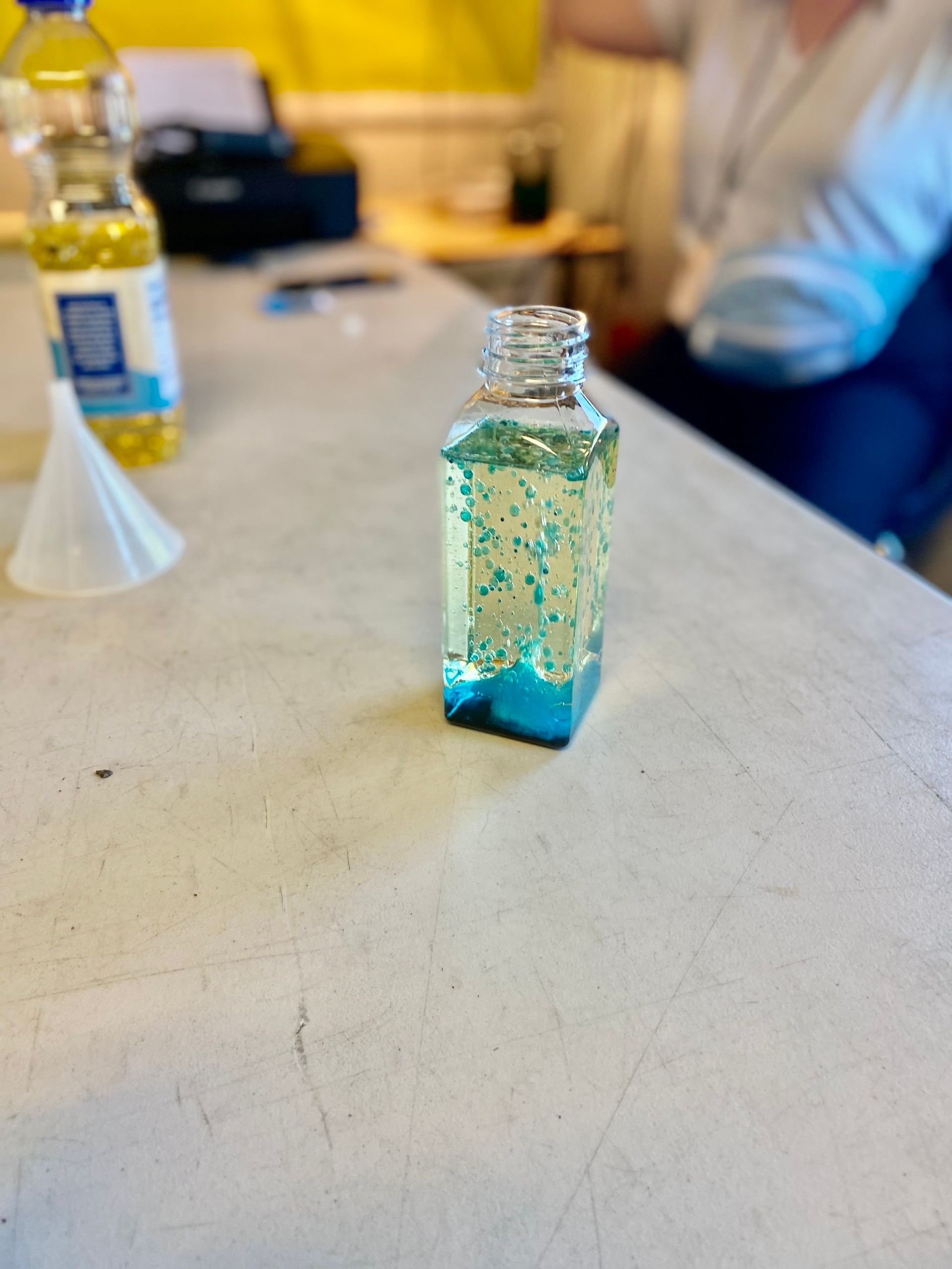 A bottle of liquid is sitting on a table next to a funnel.