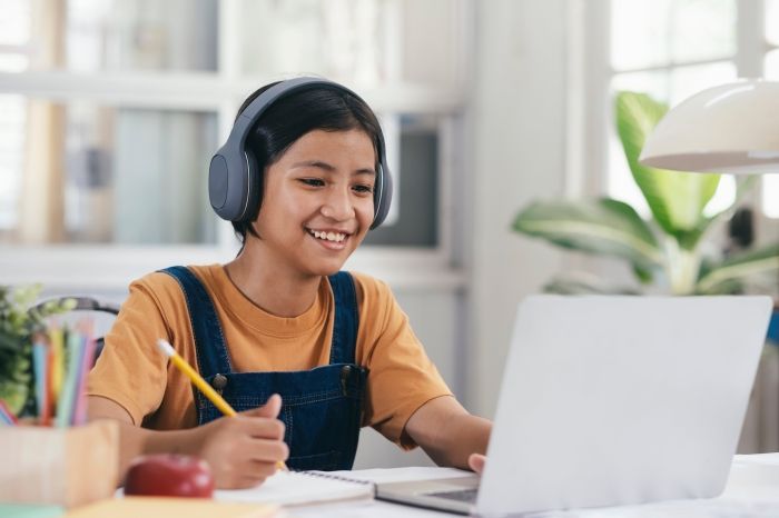 A woman is helping a little girl with her homework while using a laptop computer.