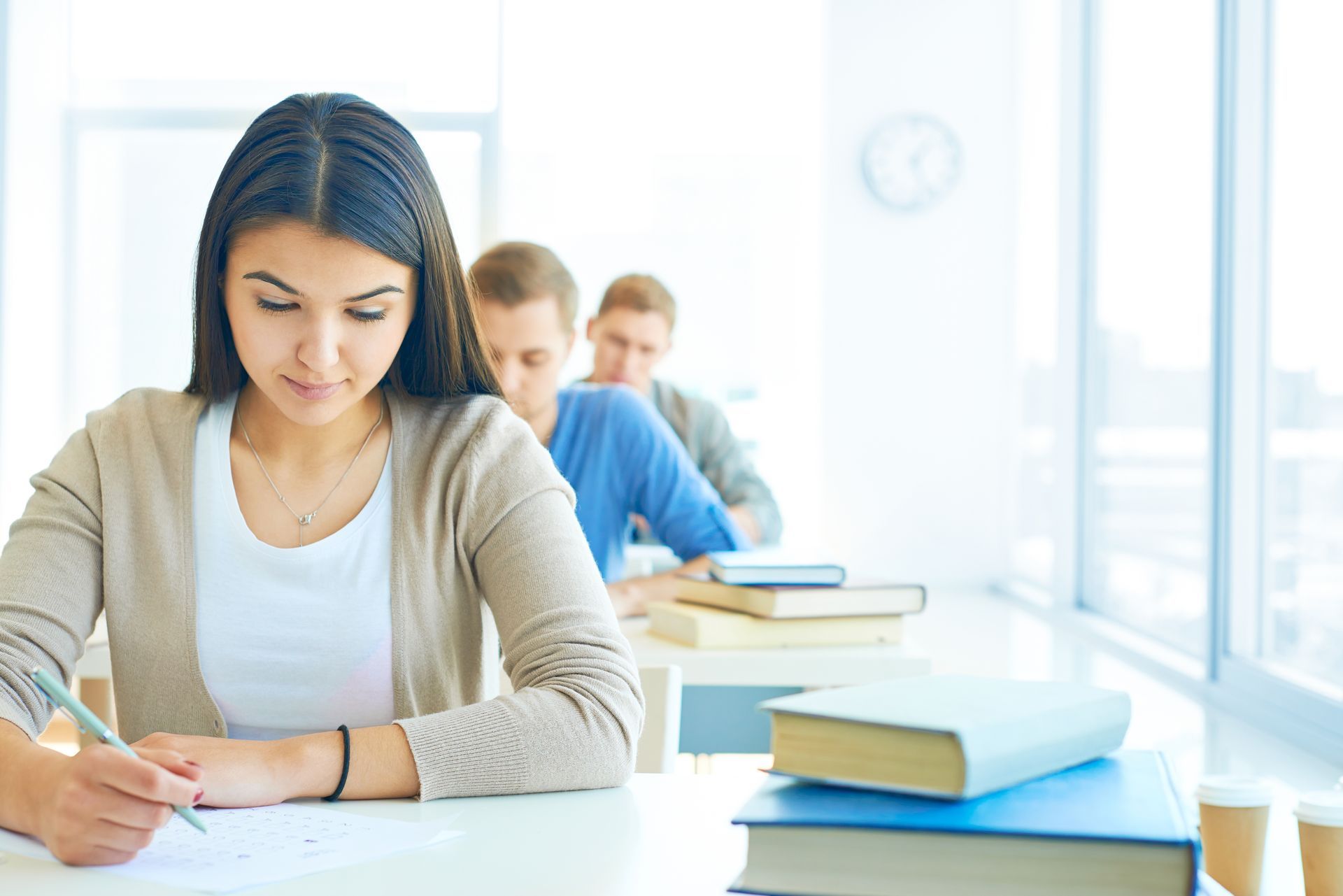 A woman is sitting at a desk in a classroom writing on a piece of paper.
