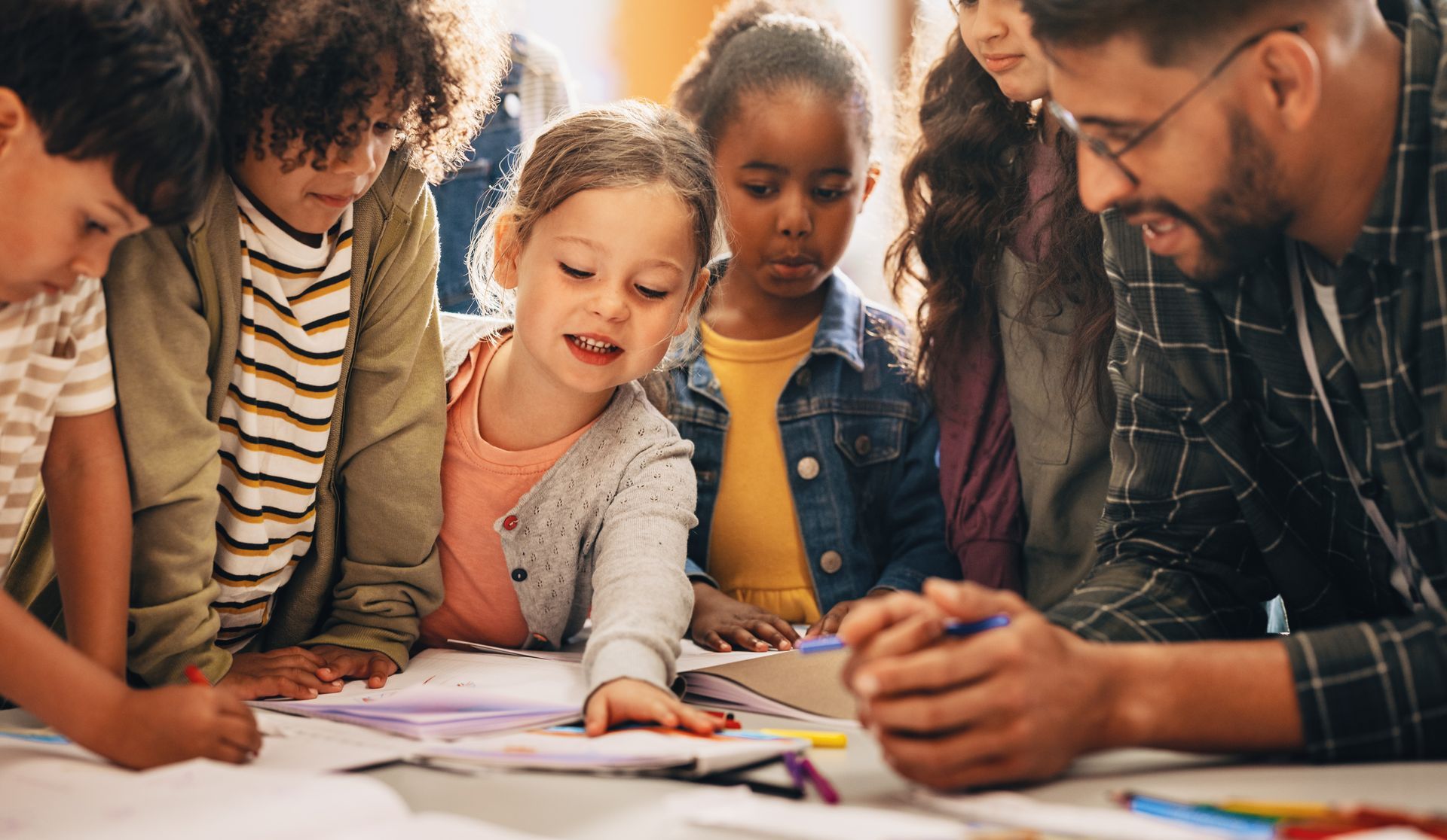 A group of children are sitting around a table with a teacher.