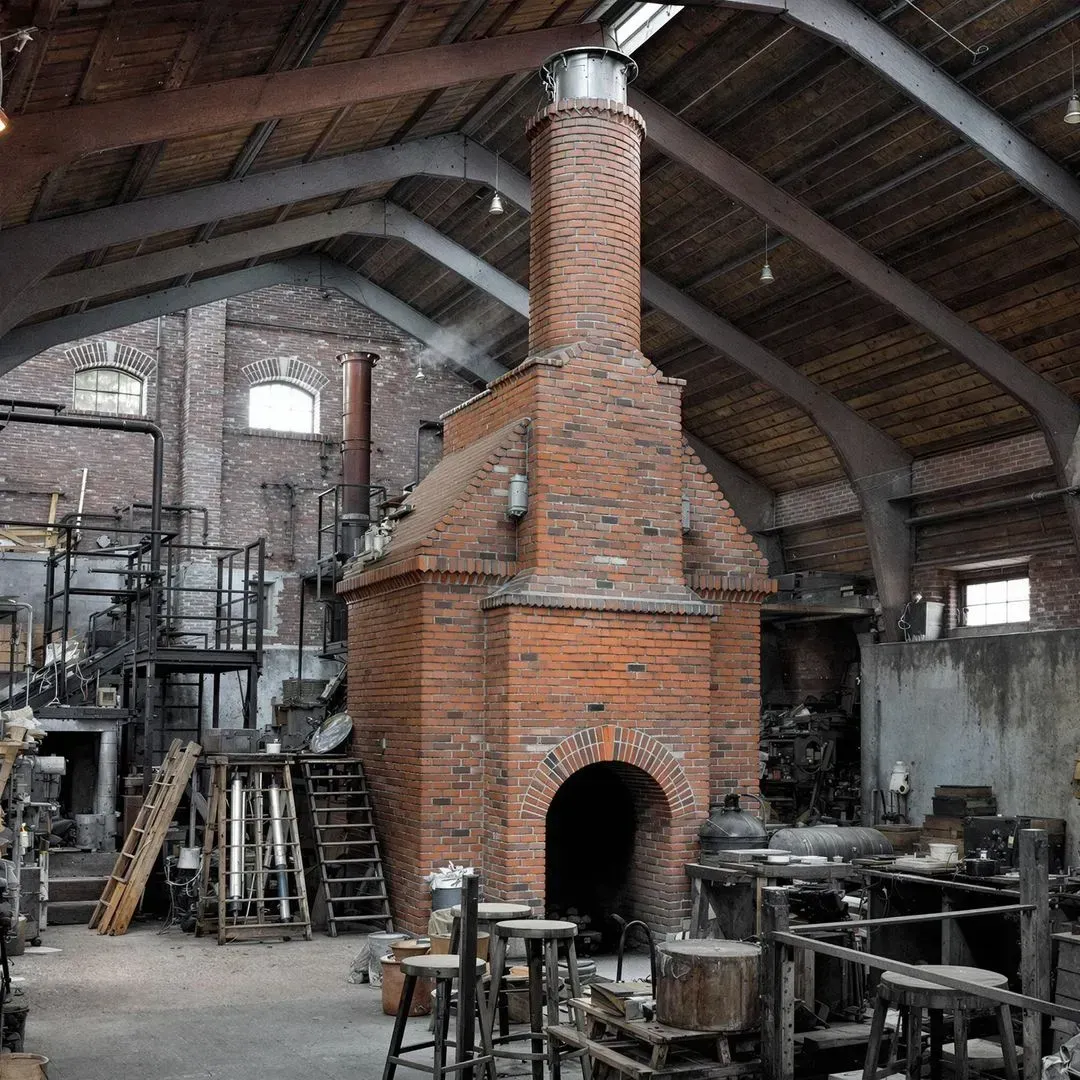 A large brick chimney is in the middle of a large room symbolizing a foundry.