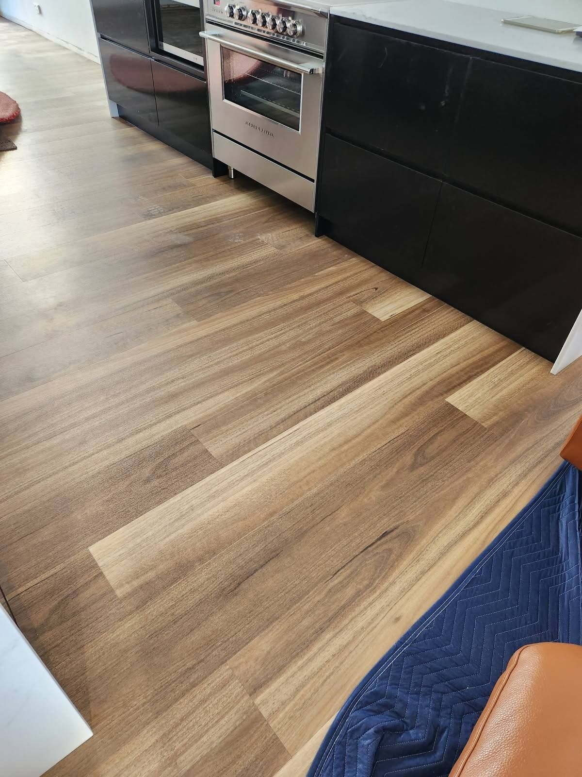 Wooden Kitchen Floor with Black Cabinets and A Silver Oven — Canberra Floor Coverings in Queanbeyan West, NSW