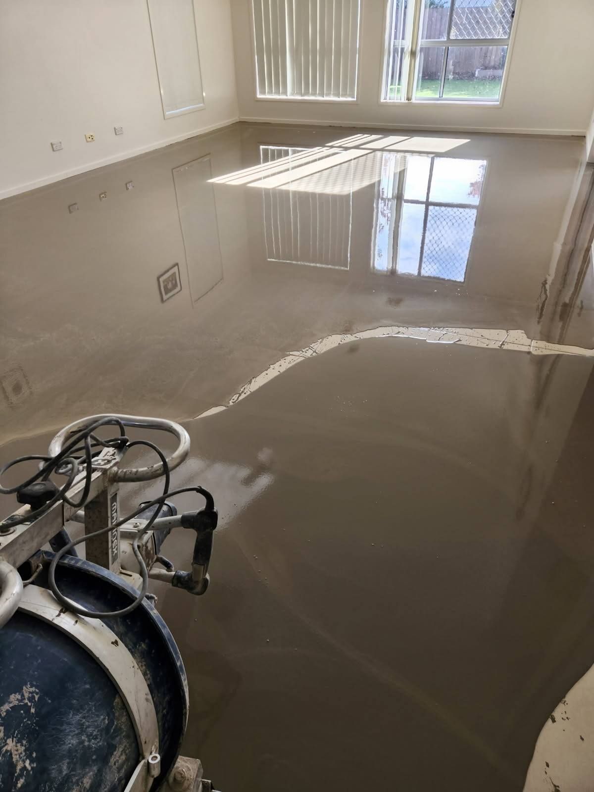 Self-Levelling Concrete Floor Being Poured in A Room; Daylight Streams Through a Window, and A Levelling Tool Is in View — Canberra Floor Coverings in Queanbeyan West, NSW