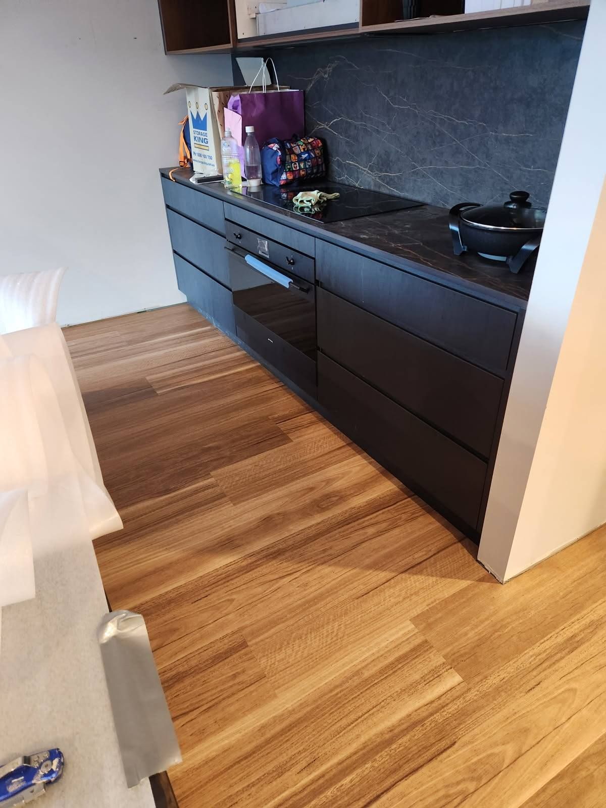 Black Kitchen Cabinets with A Black Countertop and Brown Hardwood Floors — Canberra Floor Coverings in Queanbeyan West, NSW