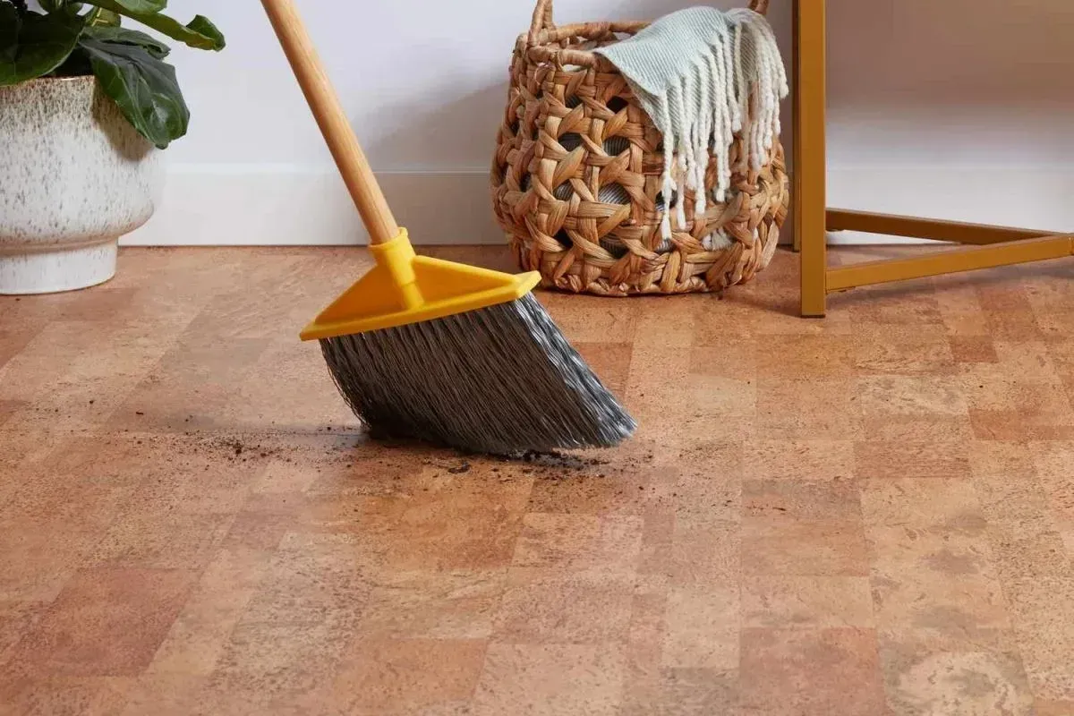 Broom Sweeping Dirt on A Cork Floor, with A Woven Basket and Plant in The Background — Canberra Floor Coverings in Queanbeyan West, NSW