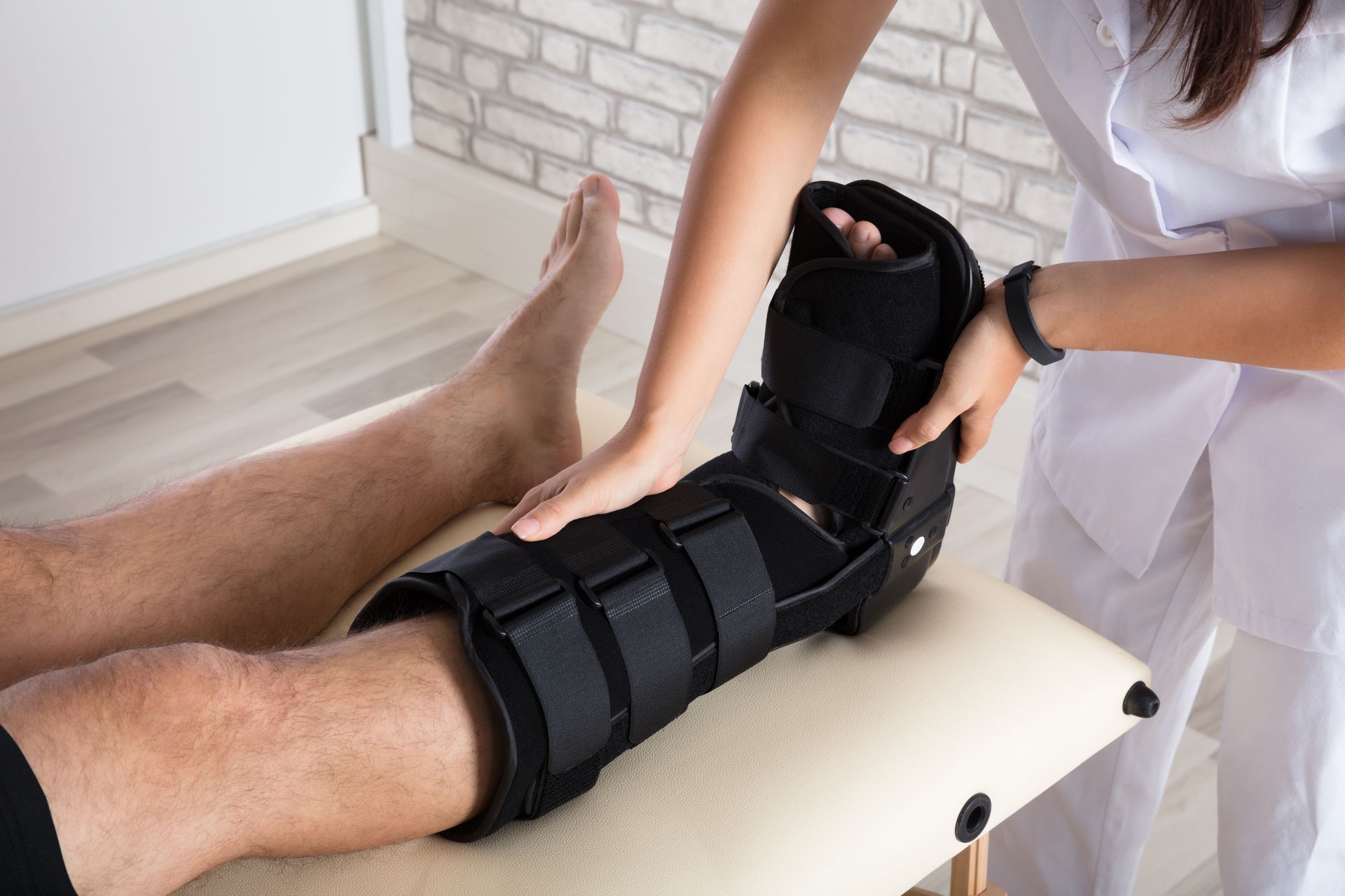 A medical professional applying a black boot brace to a patient's leg.