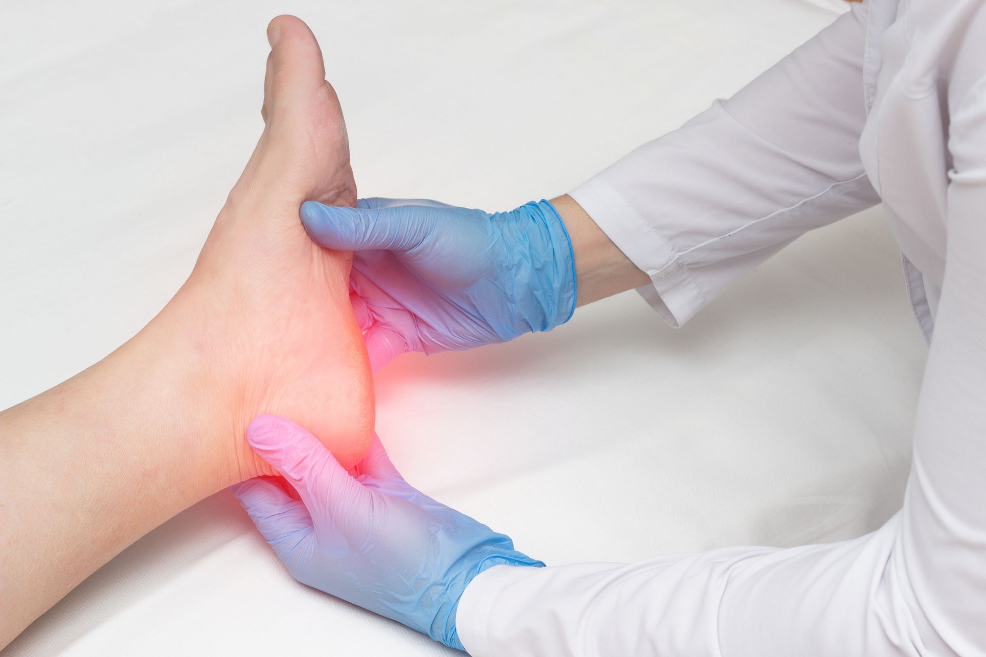 Person's ankle being examined, highlighted with red indicating pain, by someone wearing blue gloves and a white coat.