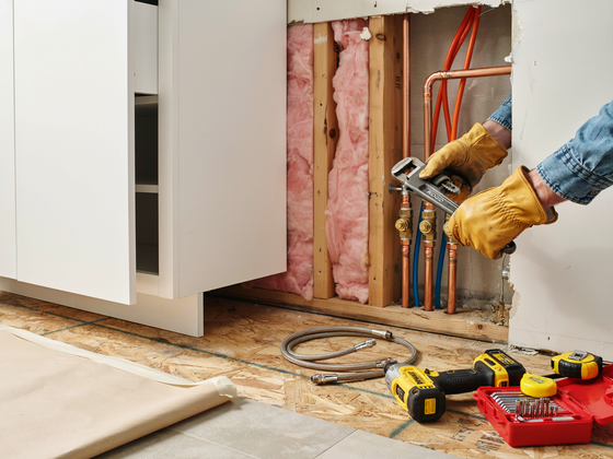 Worker installing pink insulation in a wall with tools and exposed framing in a room under renovation