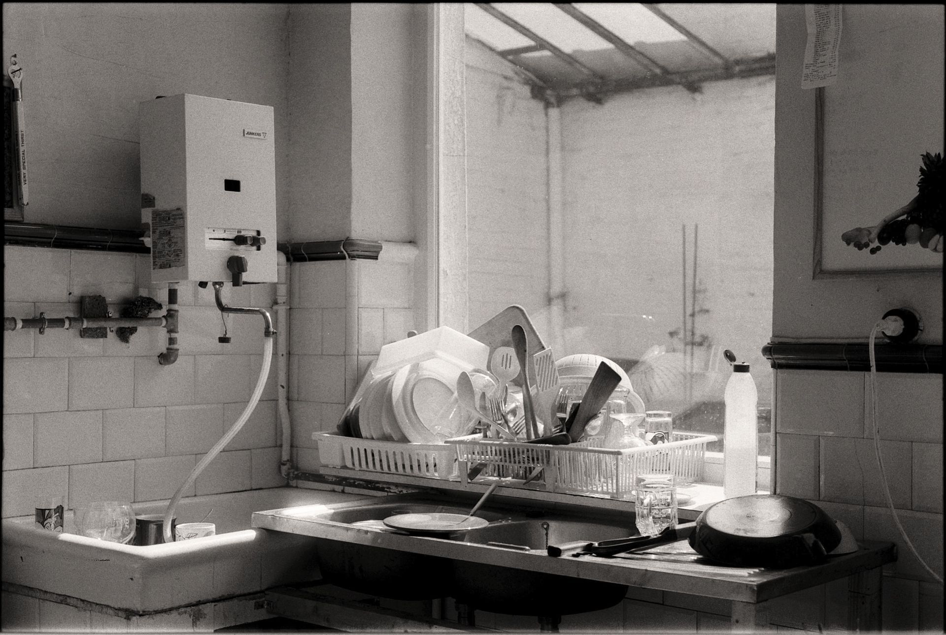 Black-and-white kitchen scene with dishes stacked in a drying rack by a sink and counter.
