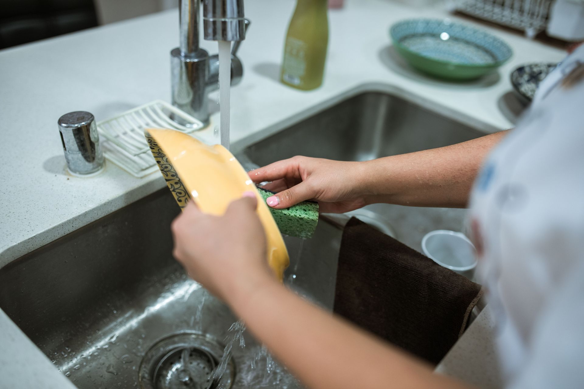 Person washing a yellow cutting board in a kitchen sink with running water