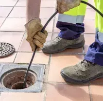 Worker clearing a clogged drain with a hose on a tiled sidewalk