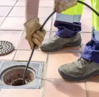 Worker clearing a clogged drain with a hose on a tiled sidewalk